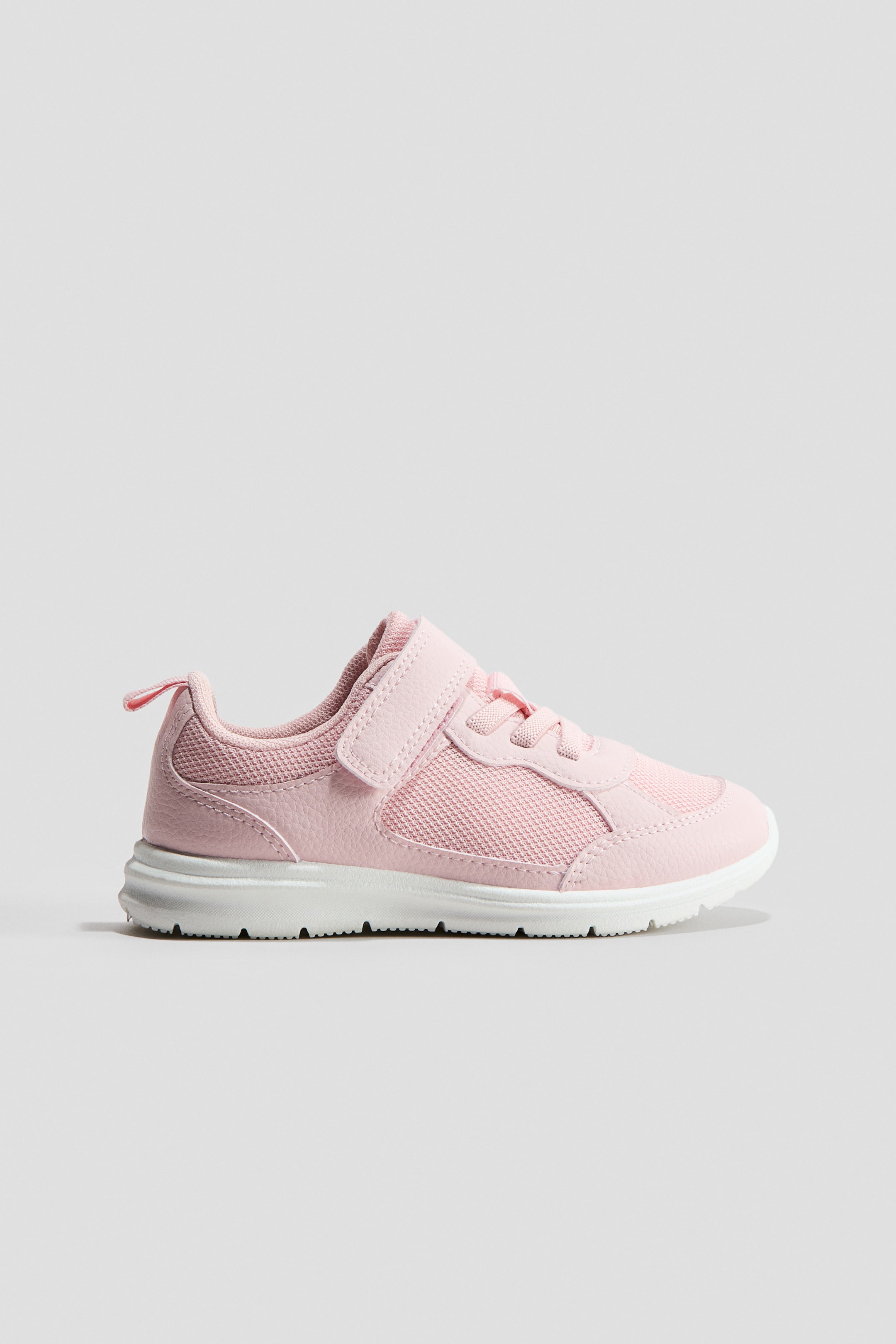 View larger image: A pink trainer is showcasing a hook and loop tab at the front, elasticated lacing, and a lightly padded edge and tongue. A grosgrain loop is appearing at the back, and the upper is featuring mesh panels along with a patterned white sole.