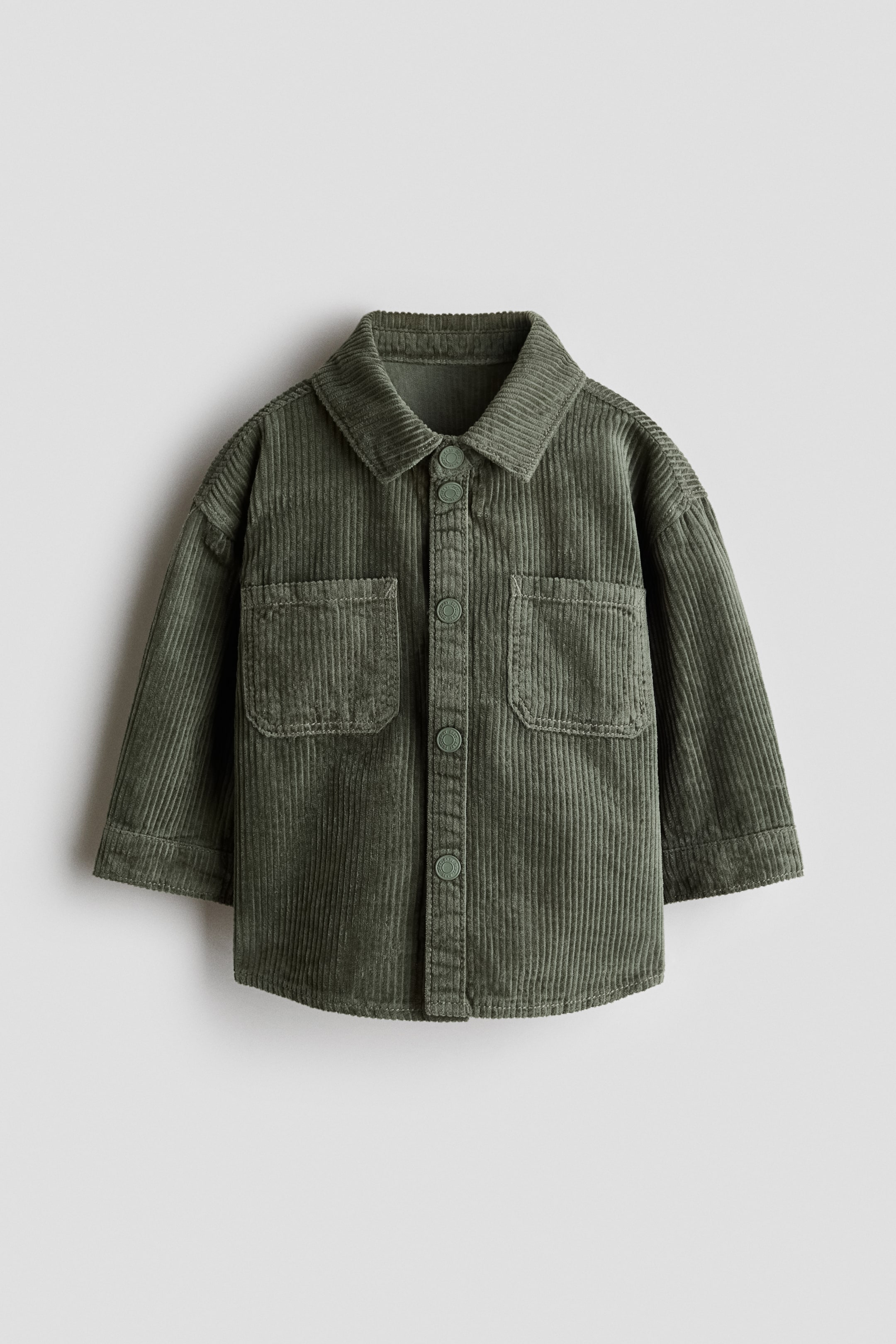 View larger image: A front-facing green corduroy shirt featuring a pointed collar and a button-up front closure with matching green buttons. It also displays two chest patch pockets with flaps and long sleeves with simple cuffs.