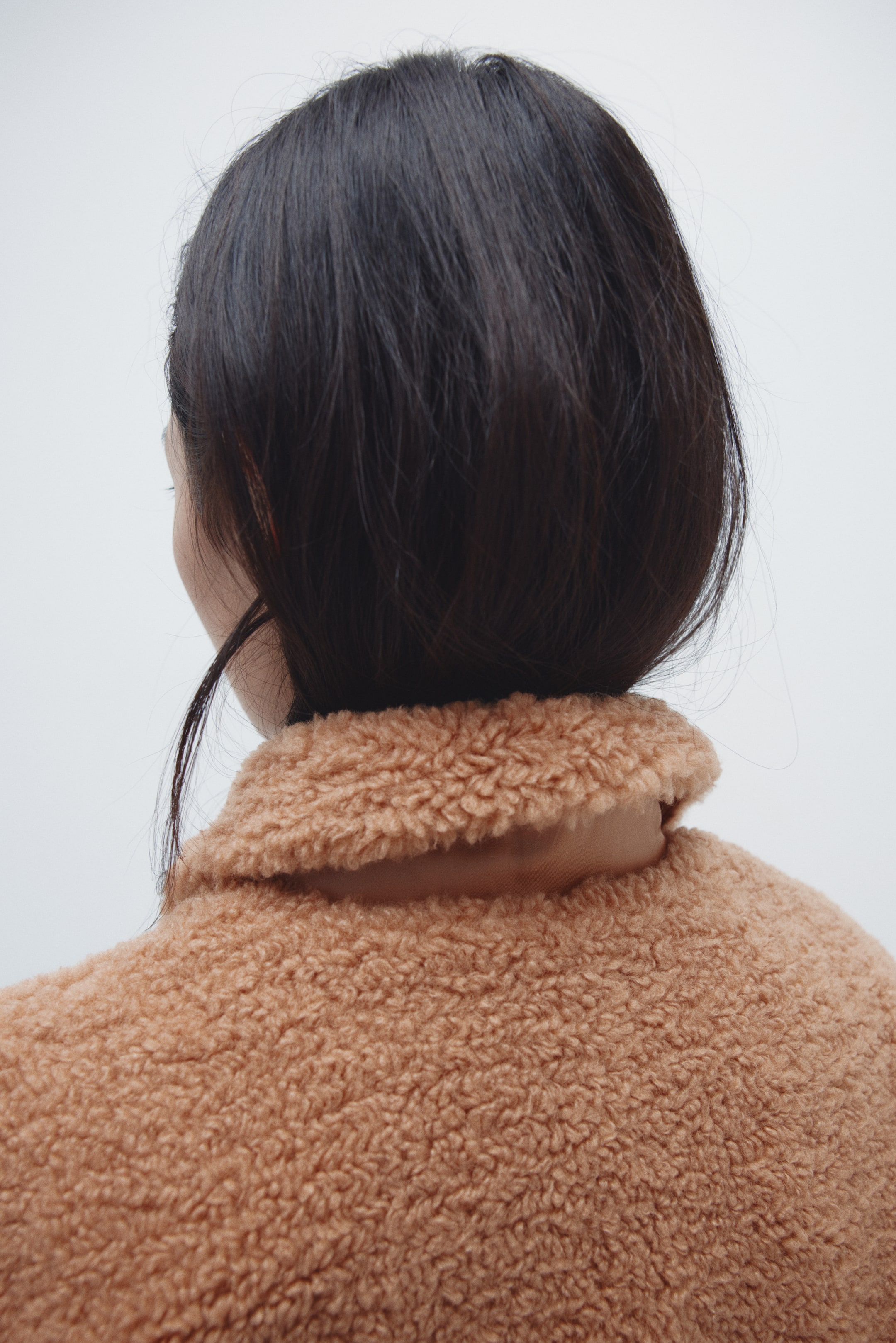 Voir une image plus grande: Un vêtement en polaire teddie de couleur chameau est vu de dos, présentant une texture douce et pelucheuse ainsi qu'un large col reposant autour du cou.