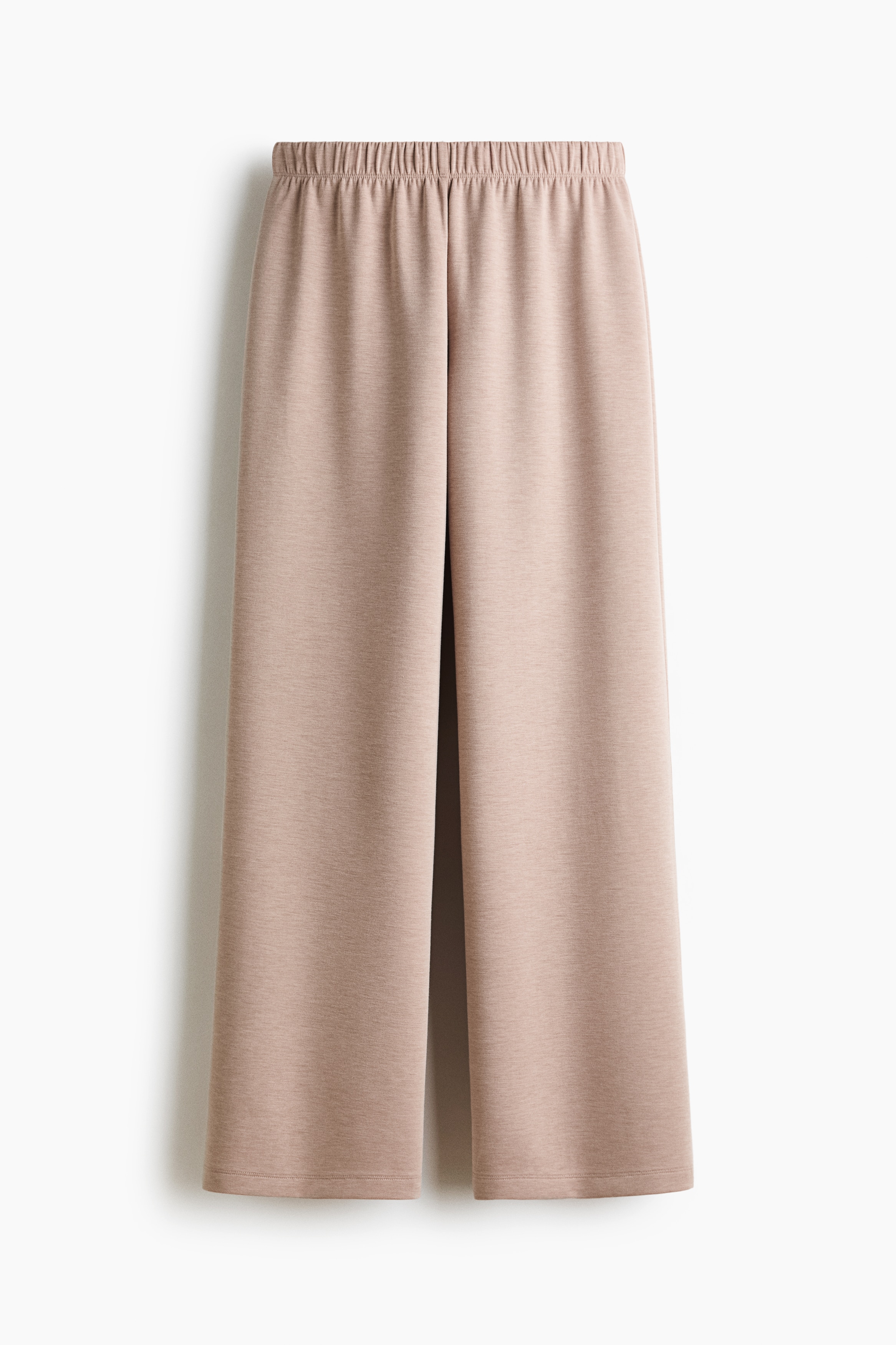 LÃ¸se bukser i beige jerseystof i viskoseblanding, med en almindelig elastisk talje og lige ben, bÃ¦res af modellen. Modellen holder en matchende langÃ¦rmet top bundet omkring buksernes talje, som er stylet med en hvid cropped T-shirt.