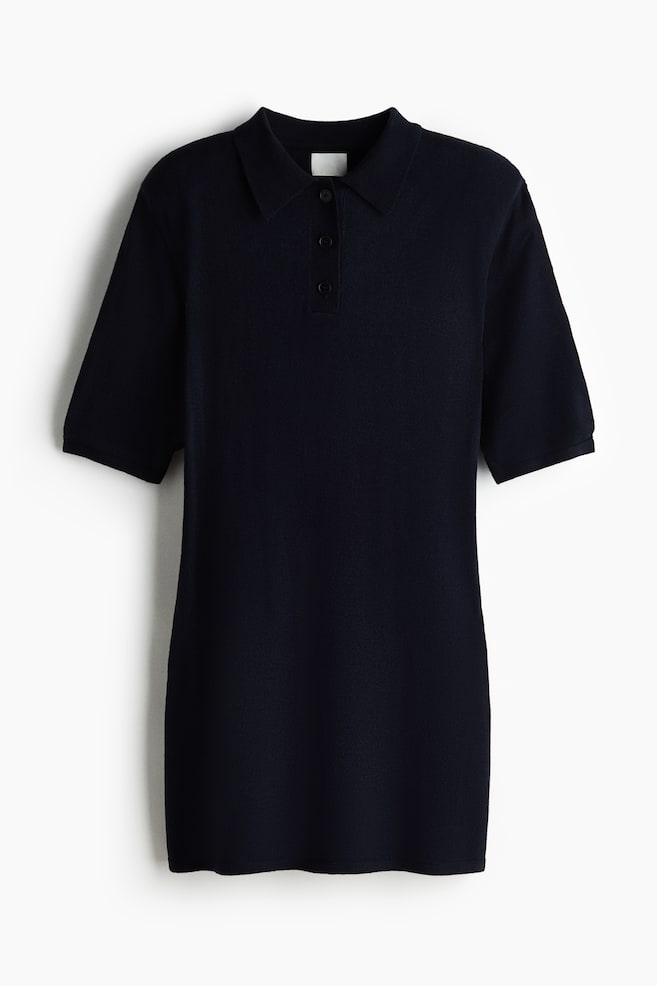 Ein marineblaues gestricktes Polokleid zeigt seine Vorderseite und verfügt über einen spitzen Kragen sowie eine Knopfleiste mit drei dunklen Knöpfen. Es ist mit kurzen Ärmeln und einem geraden Saum ausgestattet. - 1