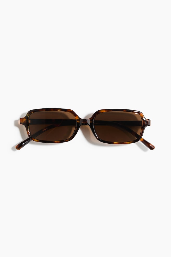 Des lunettes de soleil rectangulaires, dotées dâune monture en plastique à motif écaille de tortue brun et de verres teintés brun foncé, reposent à plat, face avant visible. - 1