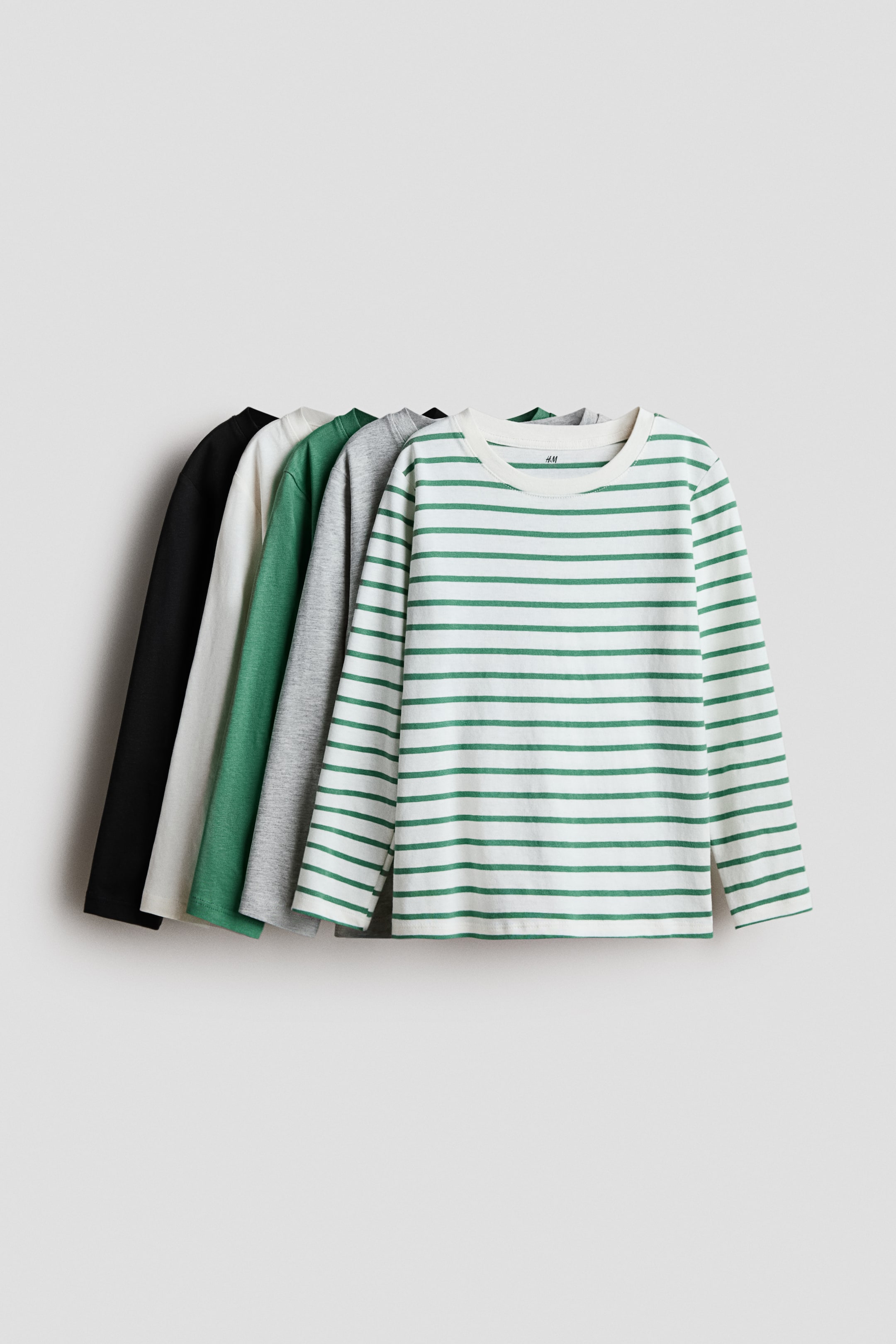 View larger image: Long-sleeved T-shirts in soft jersey are displaying, with a white and green striped shirt facing front and visible in full, while solid black, off-white, green, and grey shirts are partially layered behind it, also showing their fronts, all featuring crew necks.