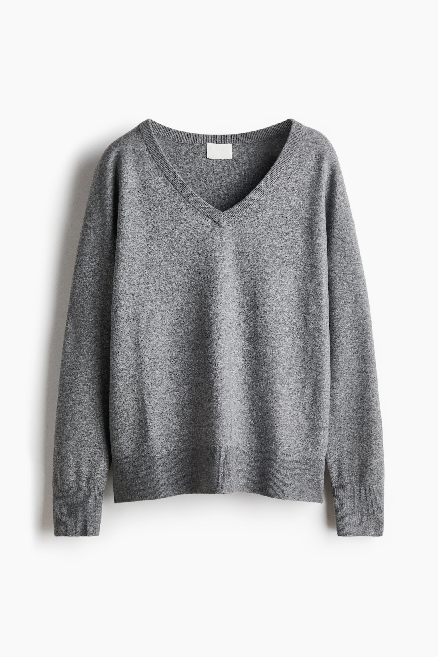 A grey V-neck jumper is showcasing a fine knit texture, with the front facing. It features a ribbed V-neckline, ribbed cuffs, and a ribbed hem, along with a small light-coloured label visible inside the back of the neck. - 1