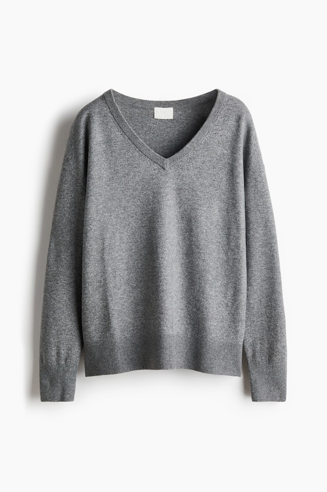 A grey V-neck sweater is displaying a fine knit texture, with the front facing. It is featuring a ribbed V-neckline, ribbed cuffs, and a ribbed hem, along with a small light-colored label visible inside the back of the neck. - 1