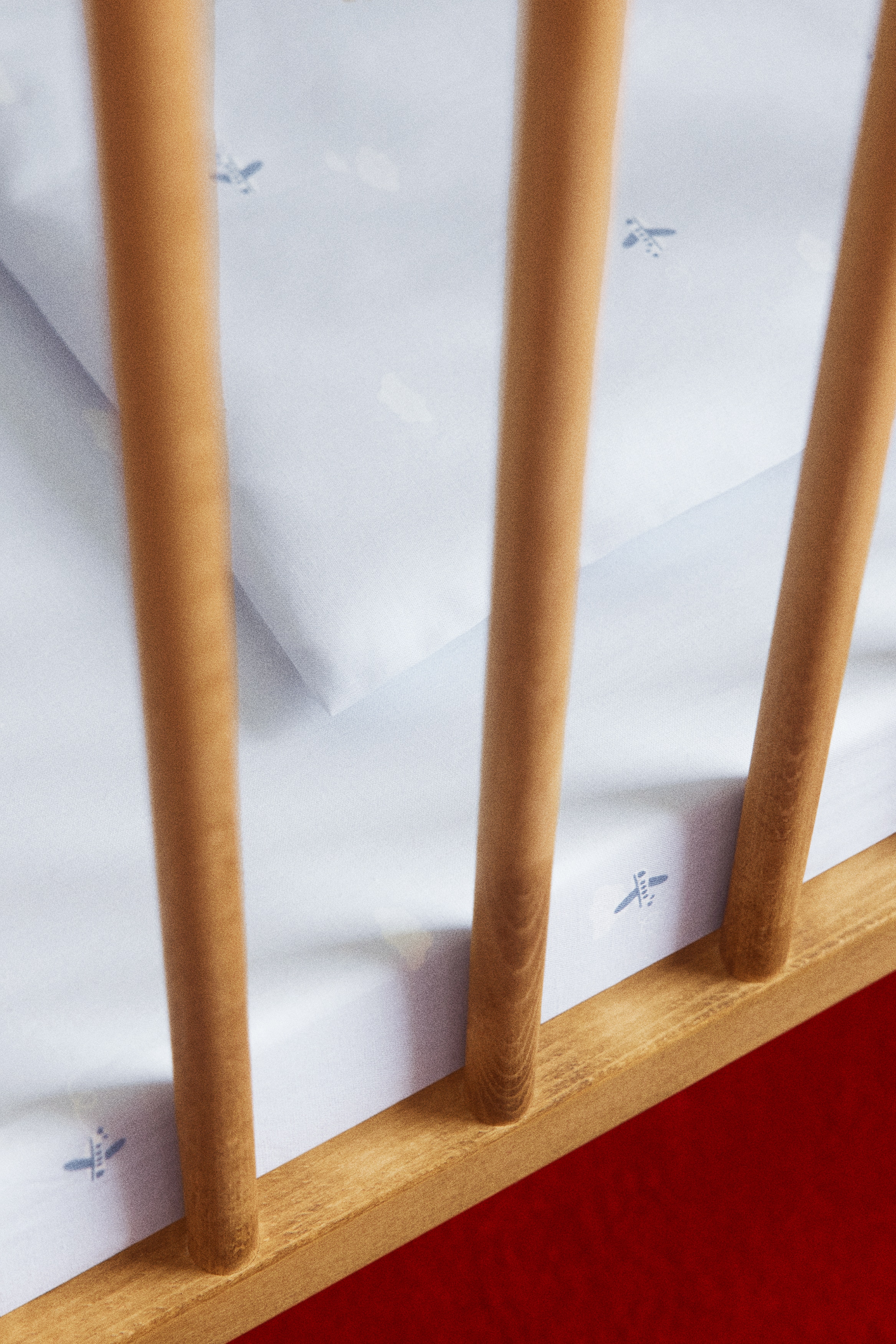 A fitted cot sheet in light blue cotton is shown covering a mattress corner from an angled view, highlighting its snug fit. The fabric features an all-over pattern of small, scattered blue airplanes and white clouds.