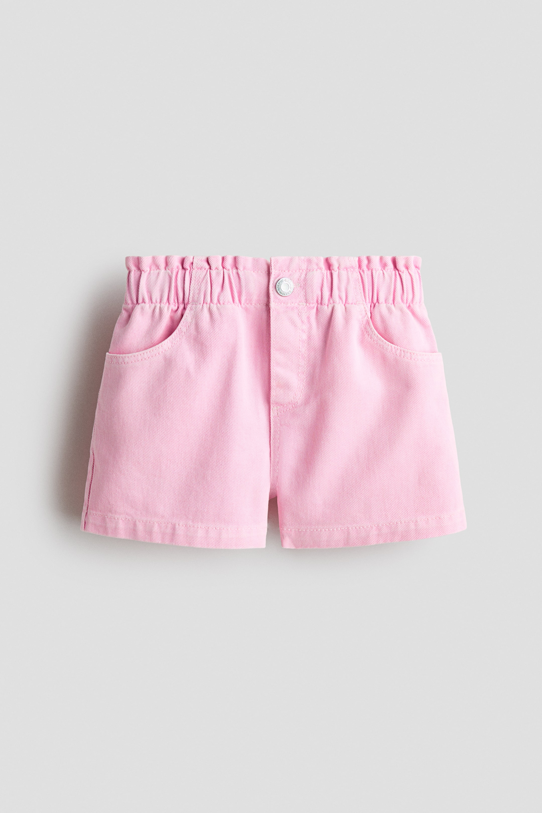 View larger image: Pink, loose-fit shorts in washed cotton denim featuring a paper bag elasticated waist, a faux fly with a centered press-stud, and diagonal front pockets.