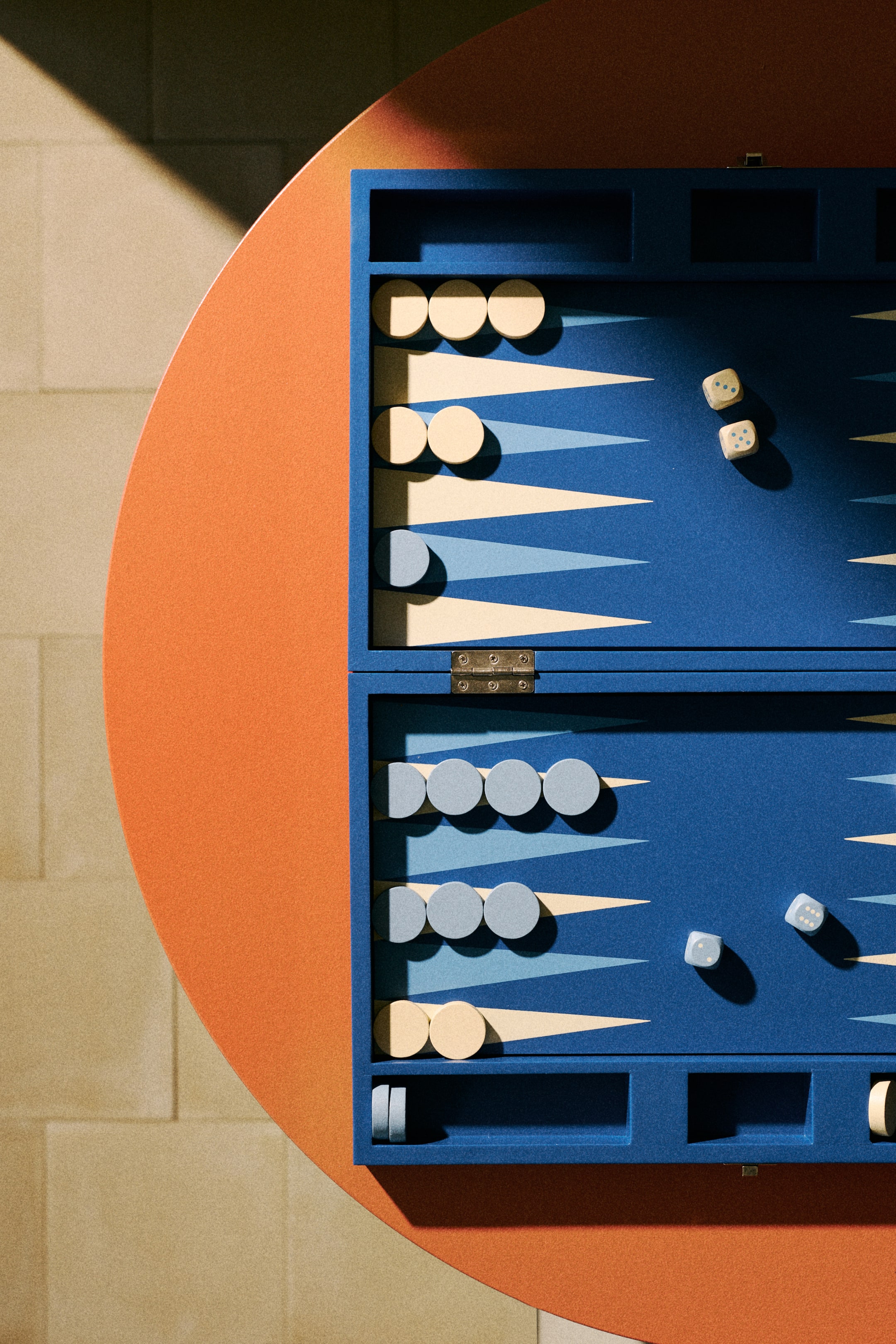 Vis større bilde: Et blått backgammon-brett presenterer krem- og lyseblå trekantede punkter. Krem- og lyseblå sirkulære brikker er arrangert på punktene og i sidebrettene, mens fire lyse terninger er spredt på spilleflaten, med tre, fem, tre og seks prikker.