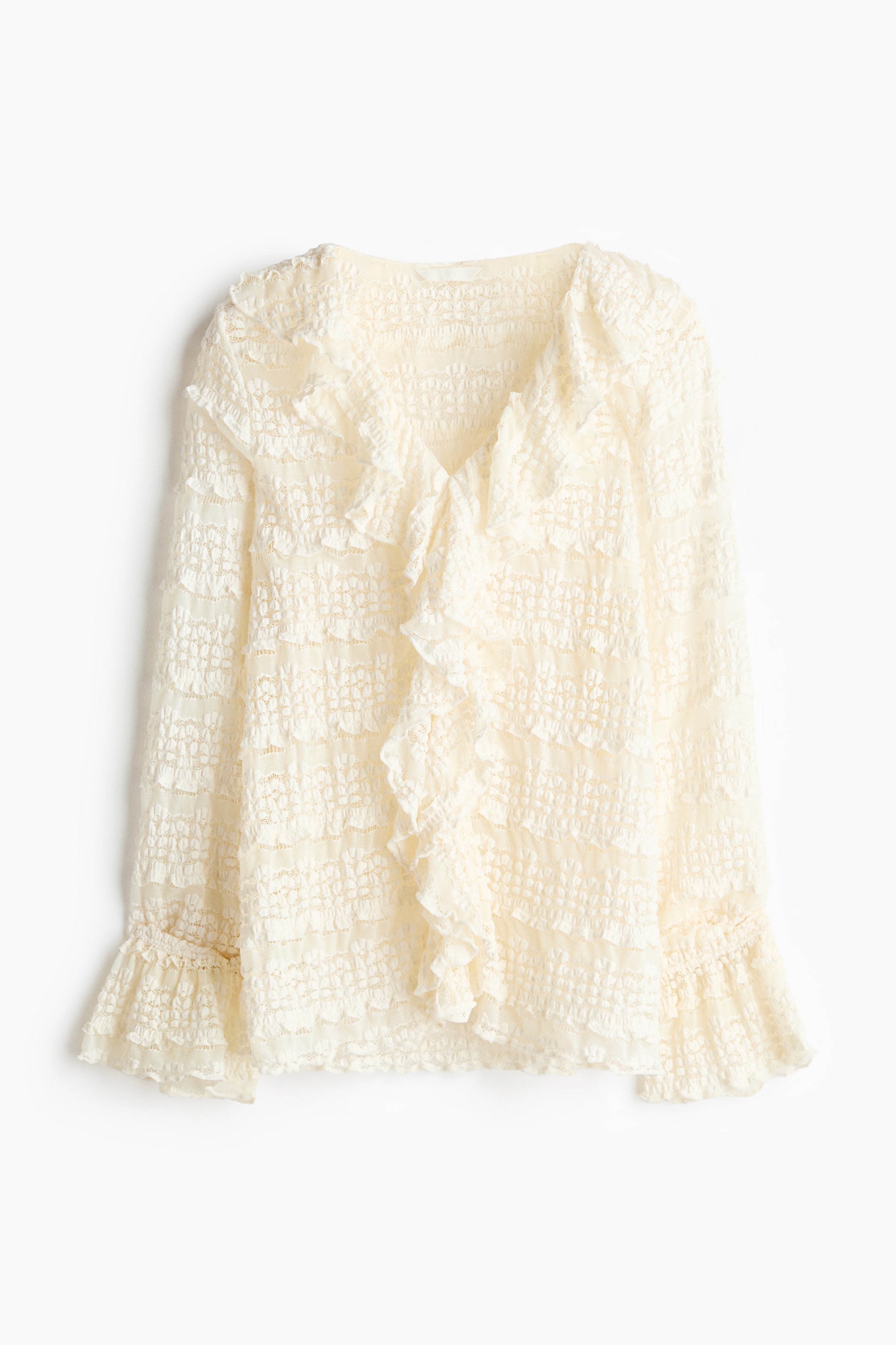 View larger image: The cream-coloured blouse showcases a textured, crinkled lace fabric, offering a V-neckline adorned with cascading ruffles along the front and long sleeves that conclude with smocked, ruffled cuffs.