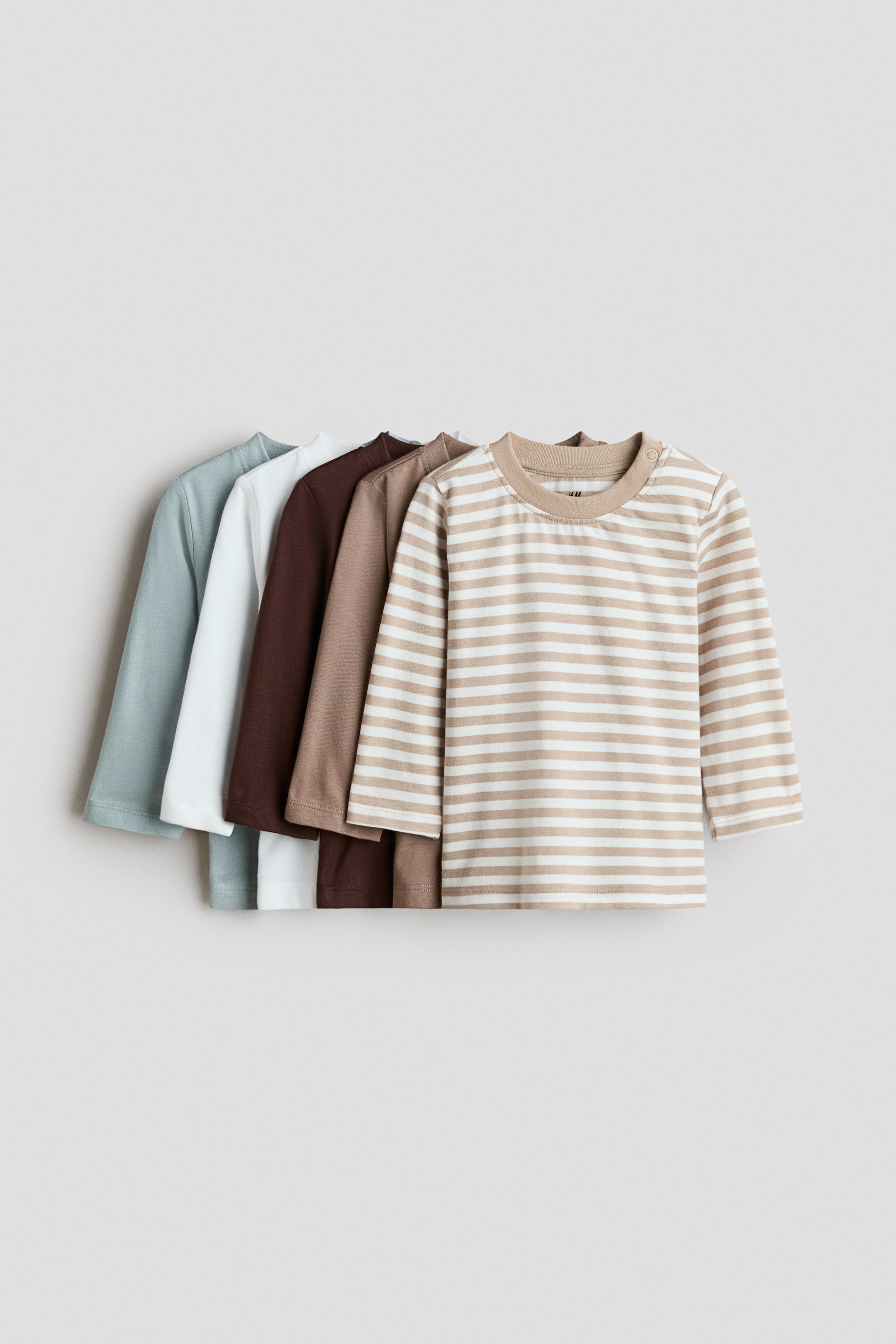 View larger image: The 5-pack cotton T-shirts are displayed as five long-sleeved shirts arranged in layers. The front shirt features beige and white horizontal stripes, a ribbed round neckline, and a snap button on the left shoulder, while the four shirts behind it are solid light brown, dark brown, white, and pale blue.
