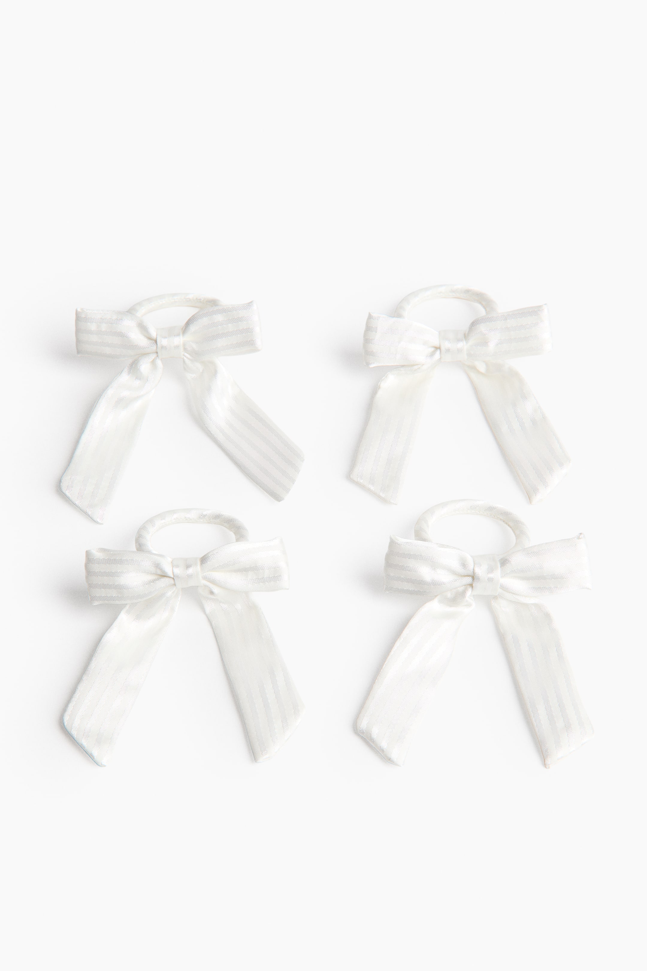 View larger image: Four white hair ties are shown from a front angle, each featuring a bow with a subtle vertical stripe pattern. The bows are tied with two loops and two tails, and the circular hair ties are covered in matching white fabric.