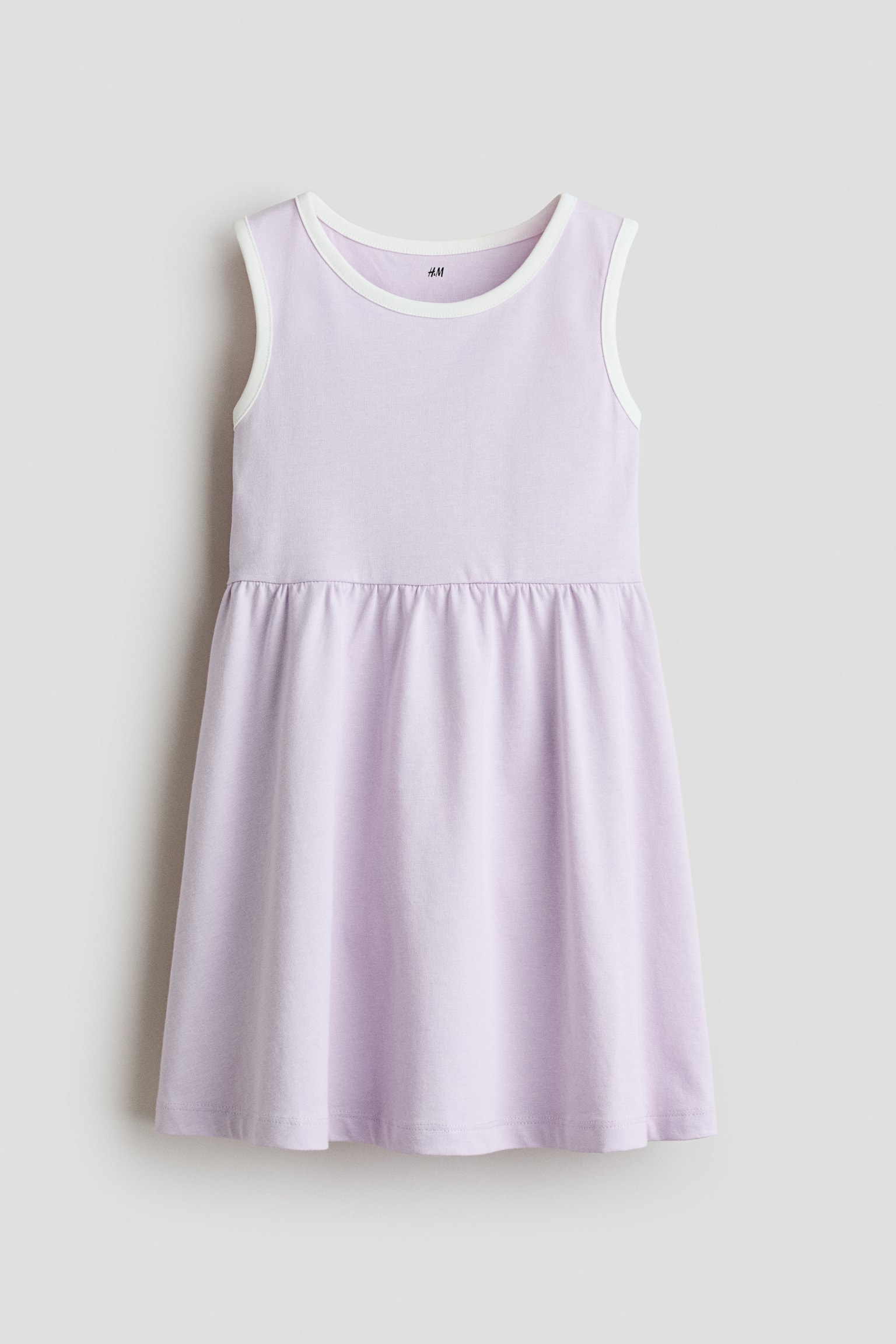 Má»t chiáº¿c vÃ¡y jersey khÃ´ng tay mÃ u tÃ­m nháº¡t ÄÆ°á»£c chá»¥p tá»« phÃ­a trÆ°á»c, ná»i báº­t vá»i ÄÆ°á»ng viá»n tráº¯ng tÆ°Æ¡ng pháº£n dá»c theo cá» trÃ²n vÃ  khoÃ©t nÃ¡ch. VÃ¡y cÃ³ ÄÆ°á»ng chiáº¿t nhÃºn táº¡i eo, chuyá»n xuá»ng chÃ¢n vÃ¡y xÃ²e.