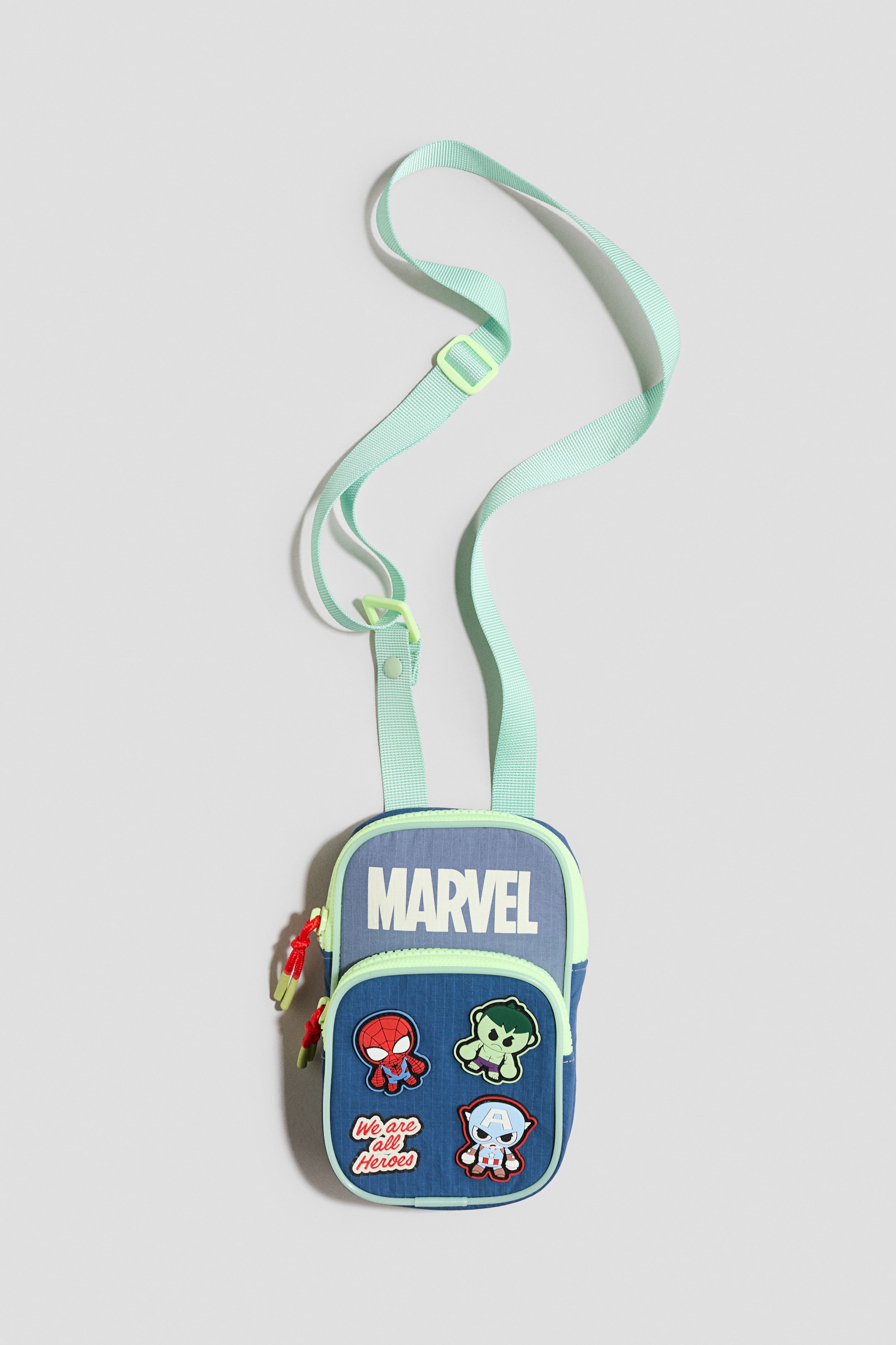 Voir une image plus grande: Un petit sac bandoulière rectangulaire Marvel est présenté de FACE, avec une section supérieure bleu clair arborant le texte "MARVEL" et une section inférieure bleu foncé. La section inférieure affiche quatre écussons de personnages et est bordée d'un passepoil jaune néon, qui encadre également la section supérieure bleu clair et s'harmonise avec la bandoulière ajustable.
