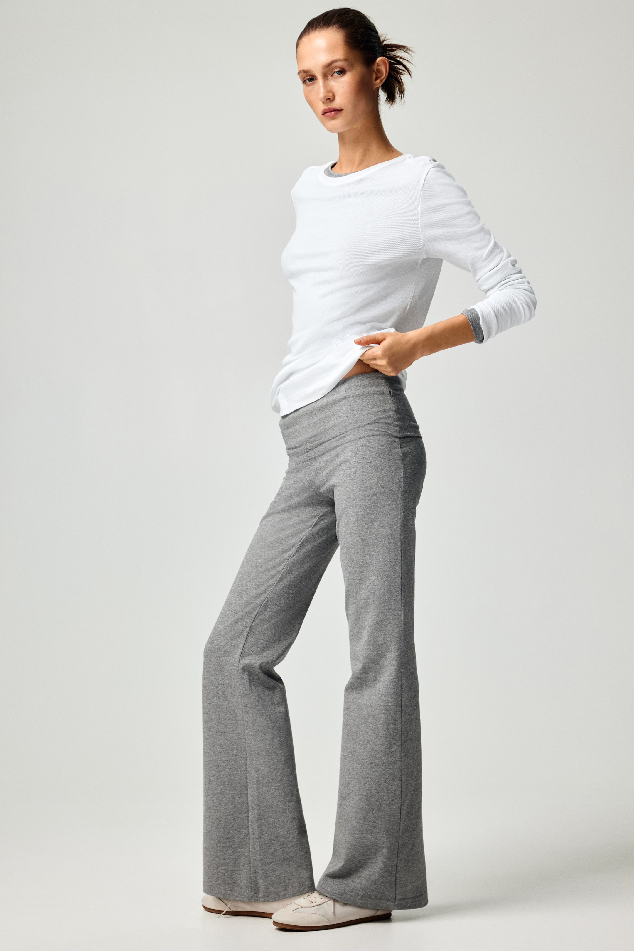 View larger image: A white long-sleeve top features a wide round neckline and long sleeves with a grey contrast trim visible at the neckline and inside the rolled cuffs. The top fits comfortably, with the hem falling over grey trousers.