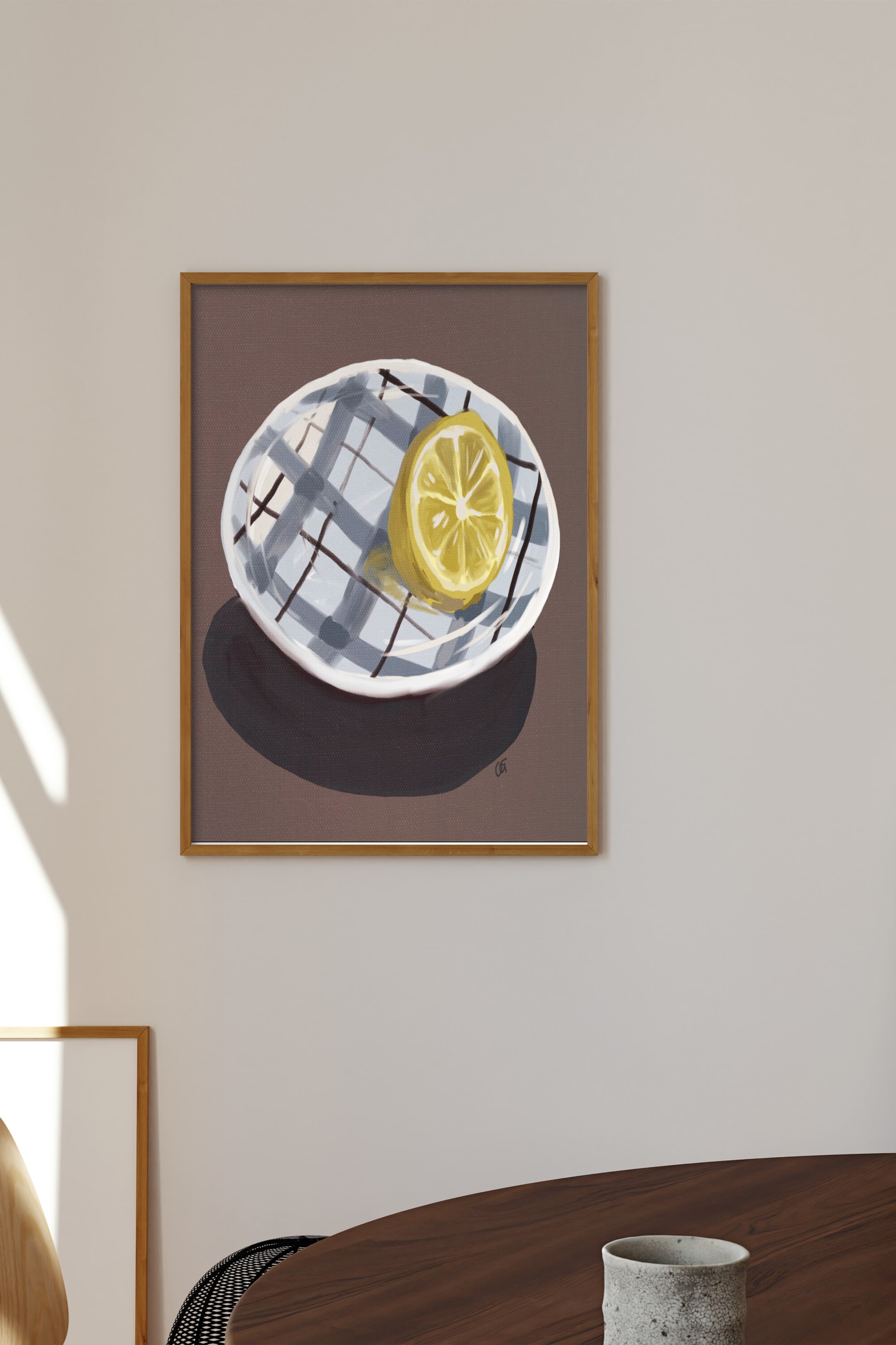 Größeres Bild ansehen: Ein gerahmtes Kunstwerk zeigt eine gelbe halbe Zitrone, die auf einem weißen Teller mit blauem und schwarzem Karomuster liegt. Das Kunstwerk verfügt über einen einfarbig dunkelbraunen Hintergrund und ist in einen hellbraunen Holzrahmen eingefasst.