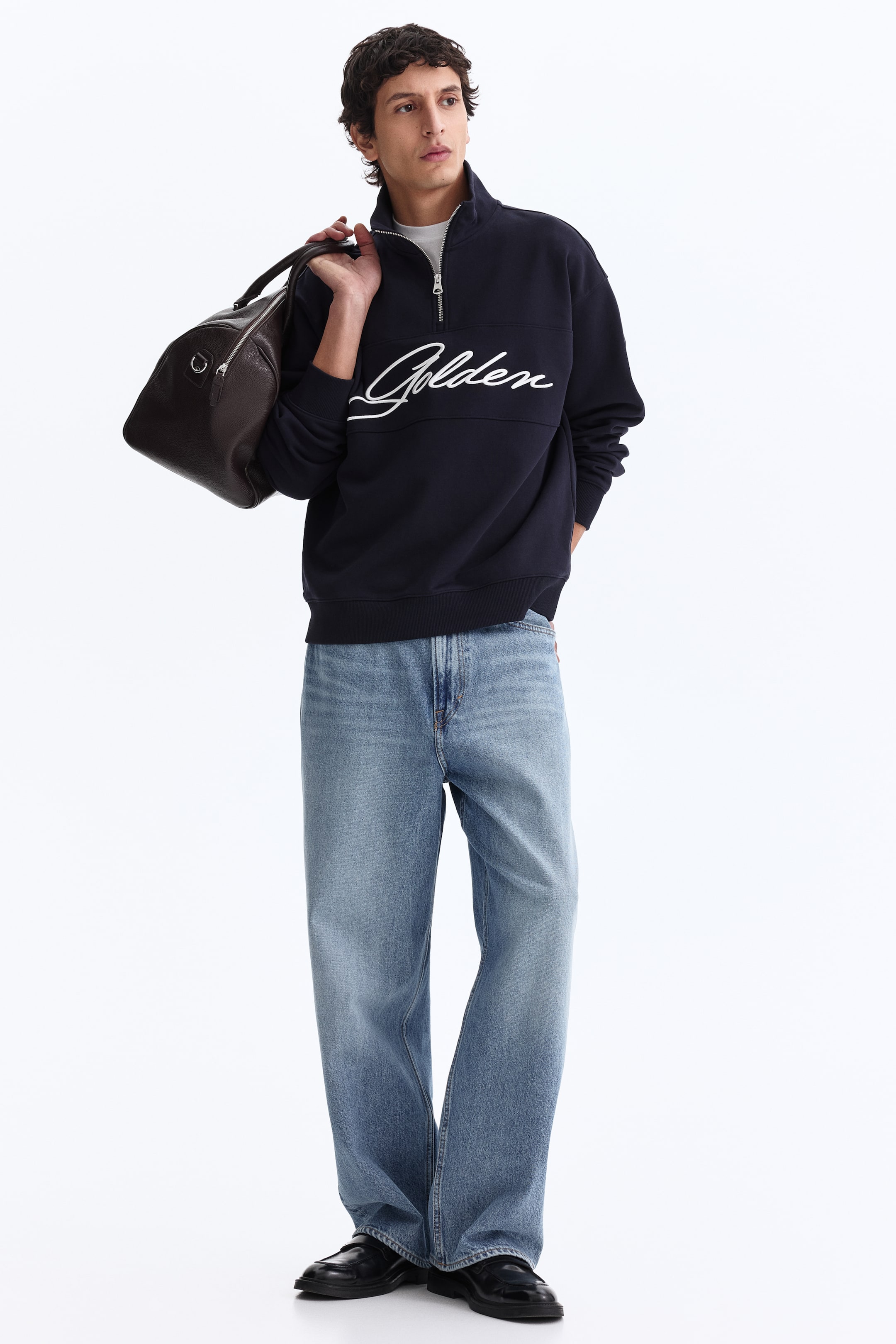 View larger image: A navy-blue quarter-zip sweatshirt is angled slightly to the right, featuring a stand-up collar and a silver-toned zip. White 'Golden' script lettering is emblazoned across the chest, and a white T-shirt is visible layered beneath the partially unzipped opening.