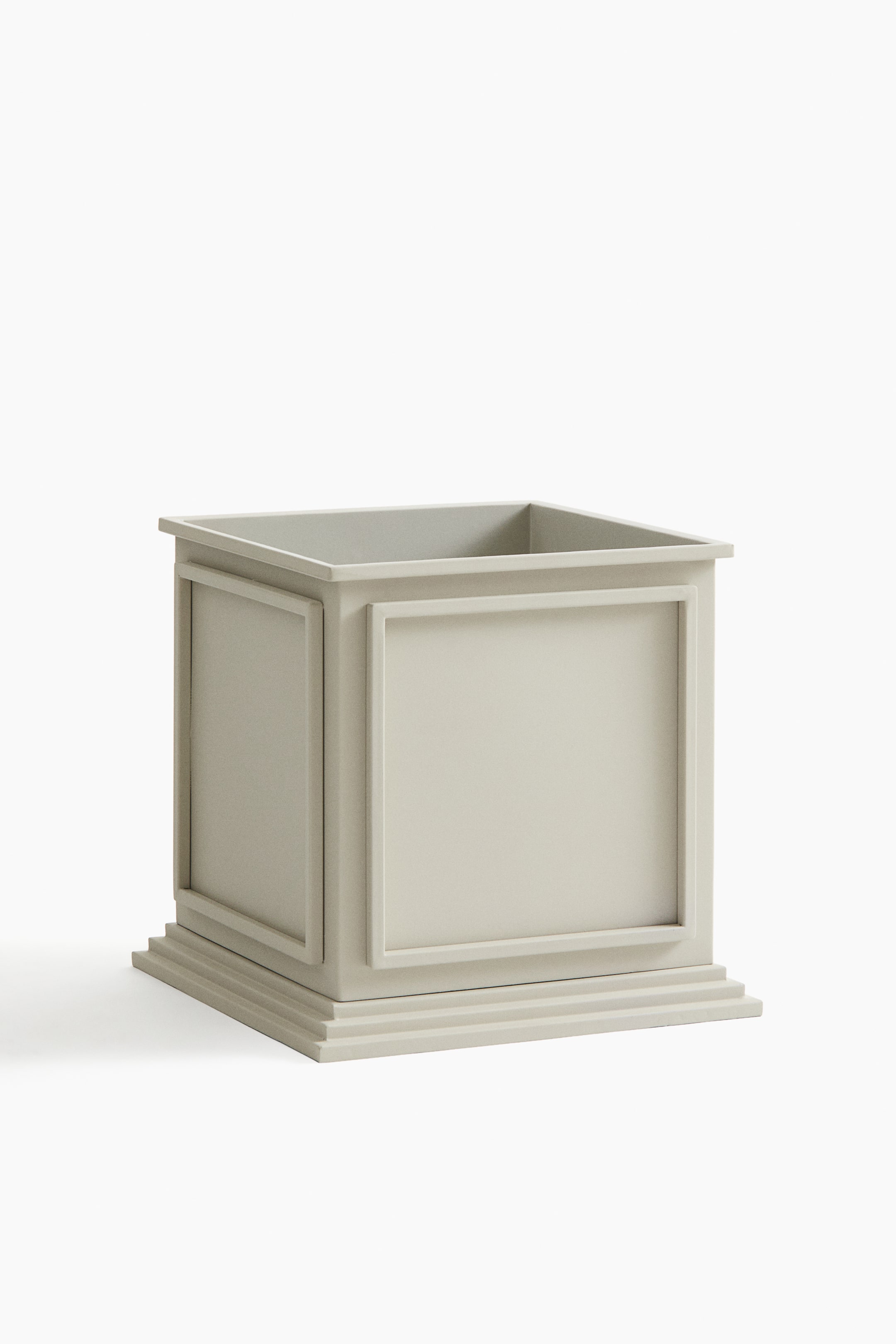 View larger image: A square metal plant pot featuring a light neutral colour, decorative framed panels on its sides, a subtle overhang at its top rim, and a multi-layered stepped base.