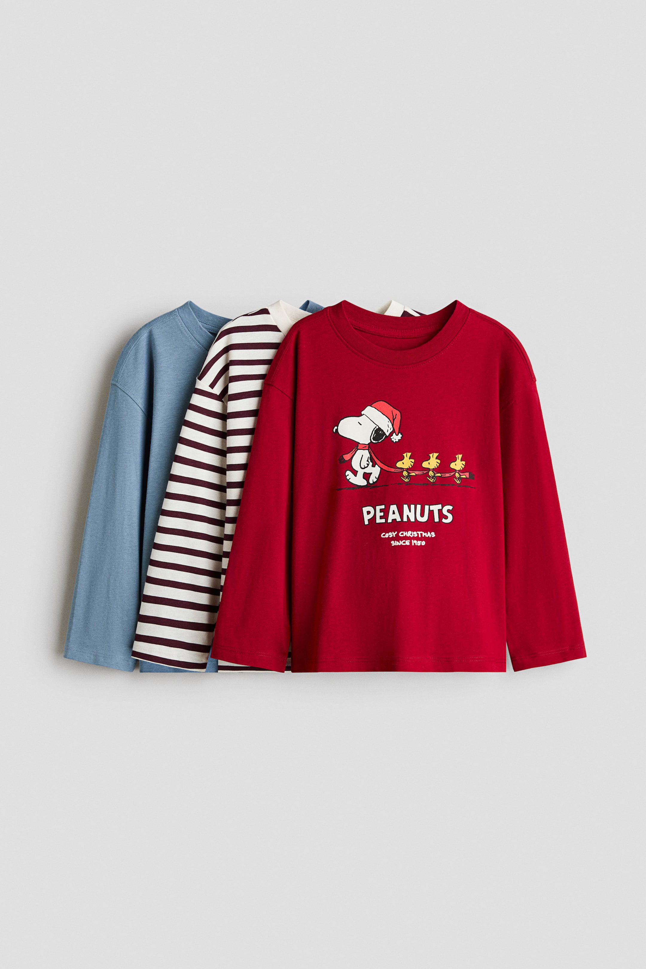 View larger image: Three long-sleeve T-shirts are displayed hanging in a layered, front-facing arrangement, featuring a solid blue tee, a white and dark red striped tee, and a red tee. The red tee in front showcases a ribbed crew neck and a printed graphic of Snoopy and Woodstock with the text "PEANUTS."