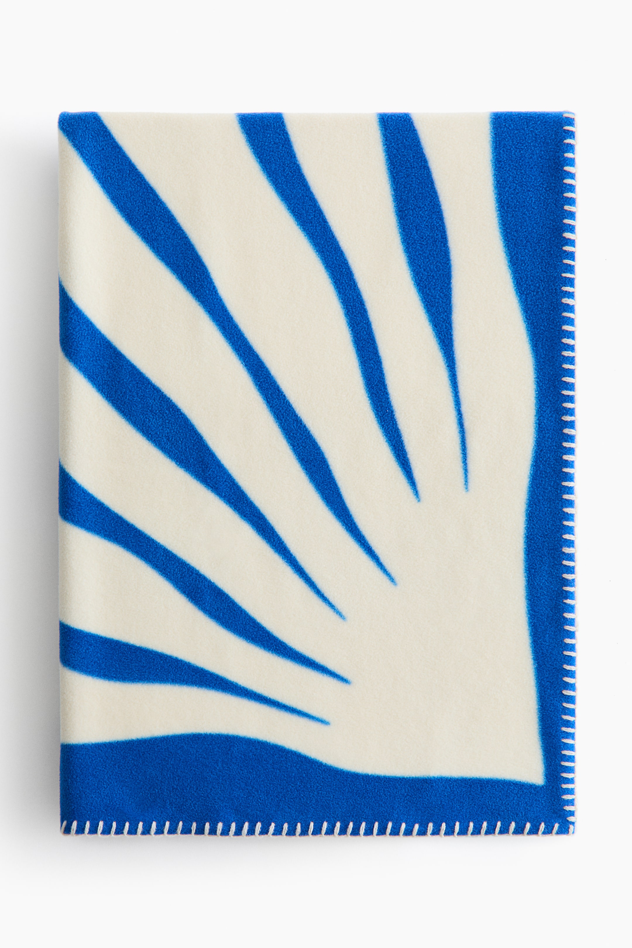 이미지 확대 보기: 플리스 담요가 정면을 보여주고 있으며, 오프 화이트 표면에 오른쪽 하단에서 방사형으로 퍼지는 넓은 파란색 줄무늬의 전체 프린트가 특징입니다. 모든 가시적인 가장자리는 흰색 담요 스티치로 세부적으로 마감되어 있습니다.