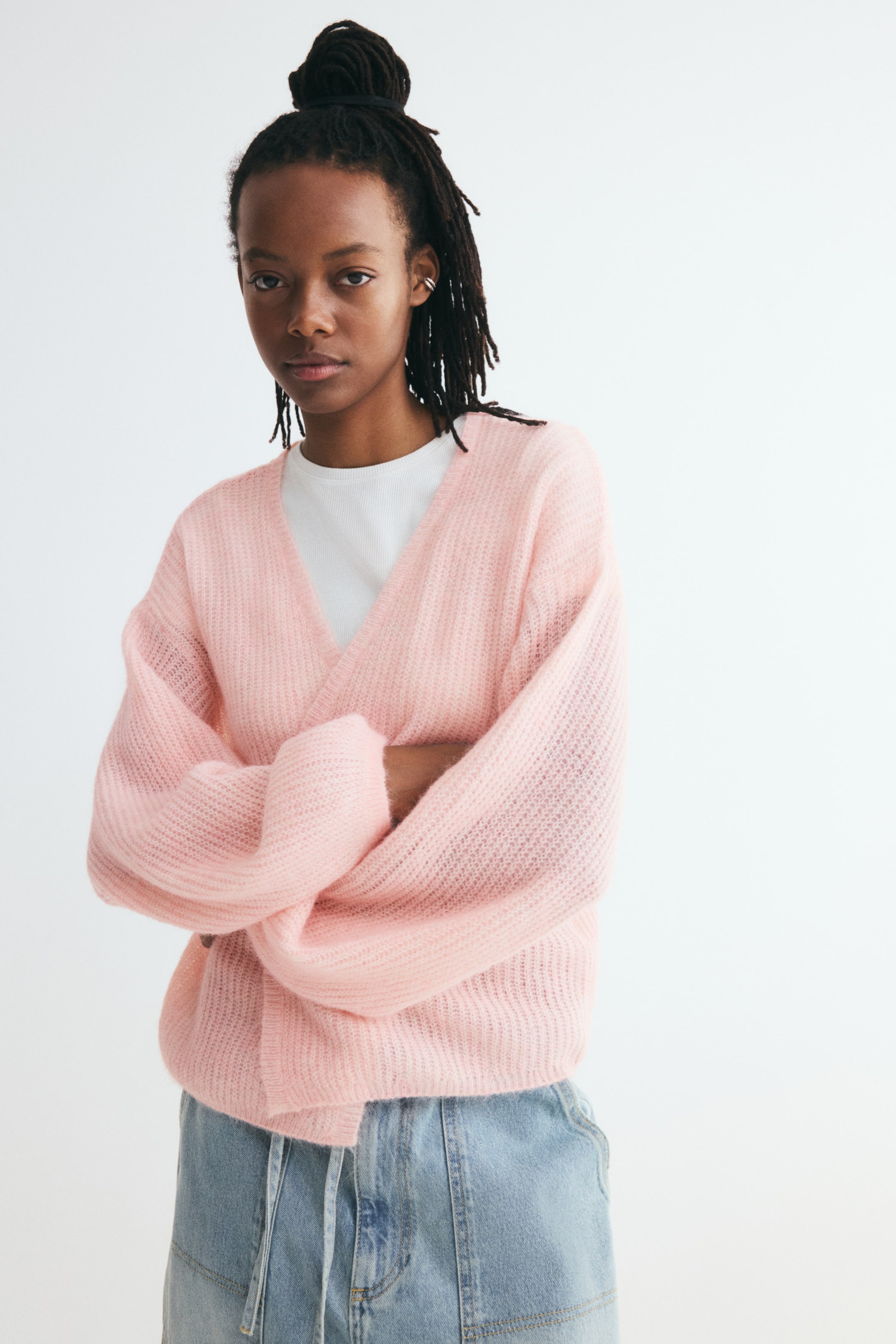 Voir une image plus grande: Ce cardigan coupe ample, rose pâle, en tricot brossé doux, est présenté de face, superposé à un t-shirt blanc à col rond. Il présente un profond décolleté en V, une ouverture sur le devant, des épaules tombantes et de longues manches ballon avec finition côtelée.