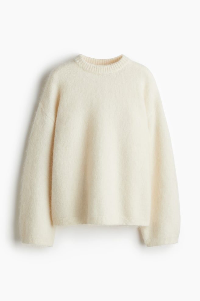 Un maglione oversize color crema è mostrato FRONTE, caratterizzato da una texture morbida e pelosa. È progettato con spalle scese, maniche lunghe e dettagli a coste sul girocollo, polsini e orlo. - 1