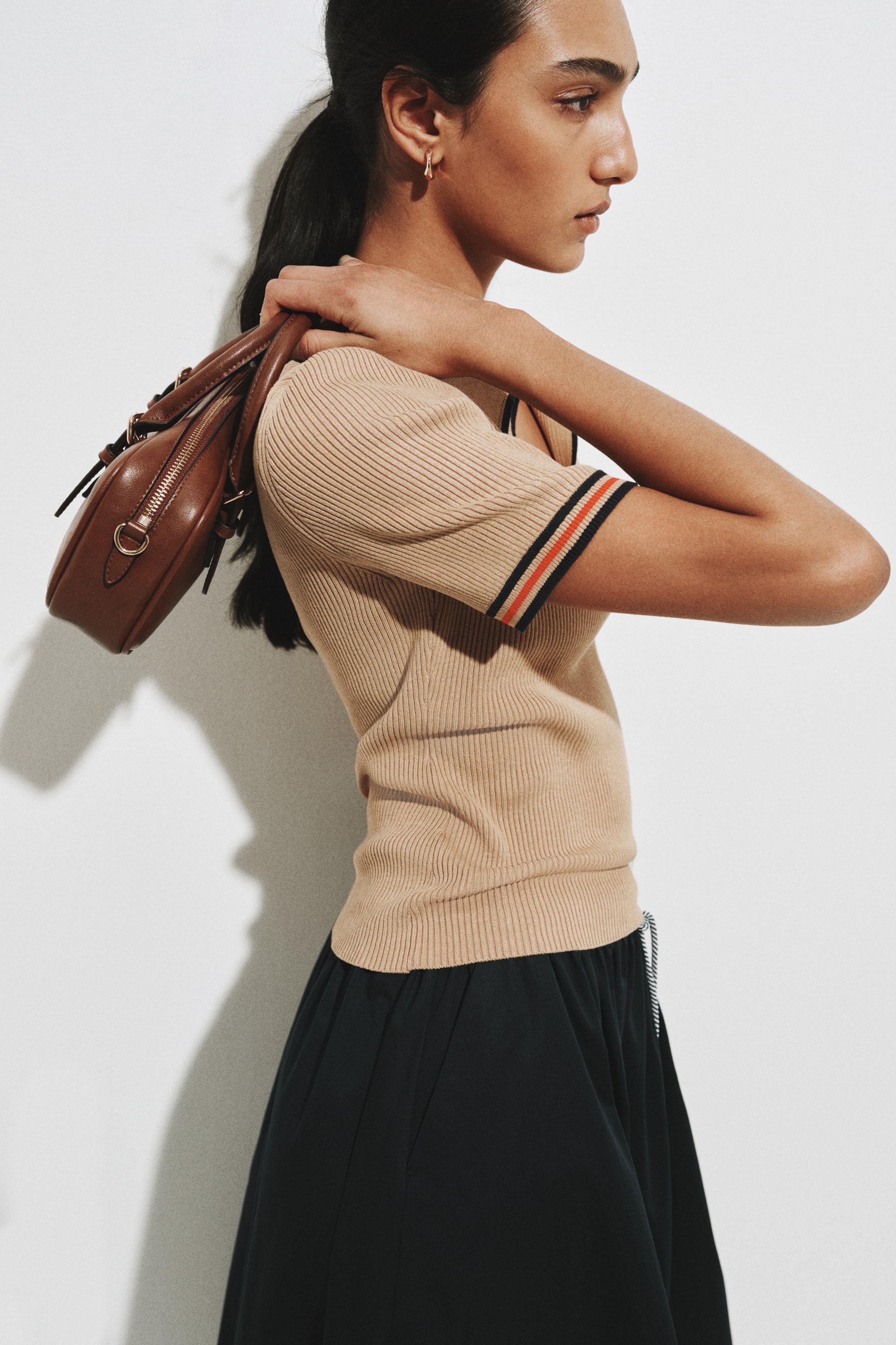 查看大圖: 一件淺棕色短袖上衣，以羅紋針織結構呈現，袖口飾以黑、橙及白色條紋，下擺為羅紋設計，從側面角度顯現貼身剪裁輪廓。