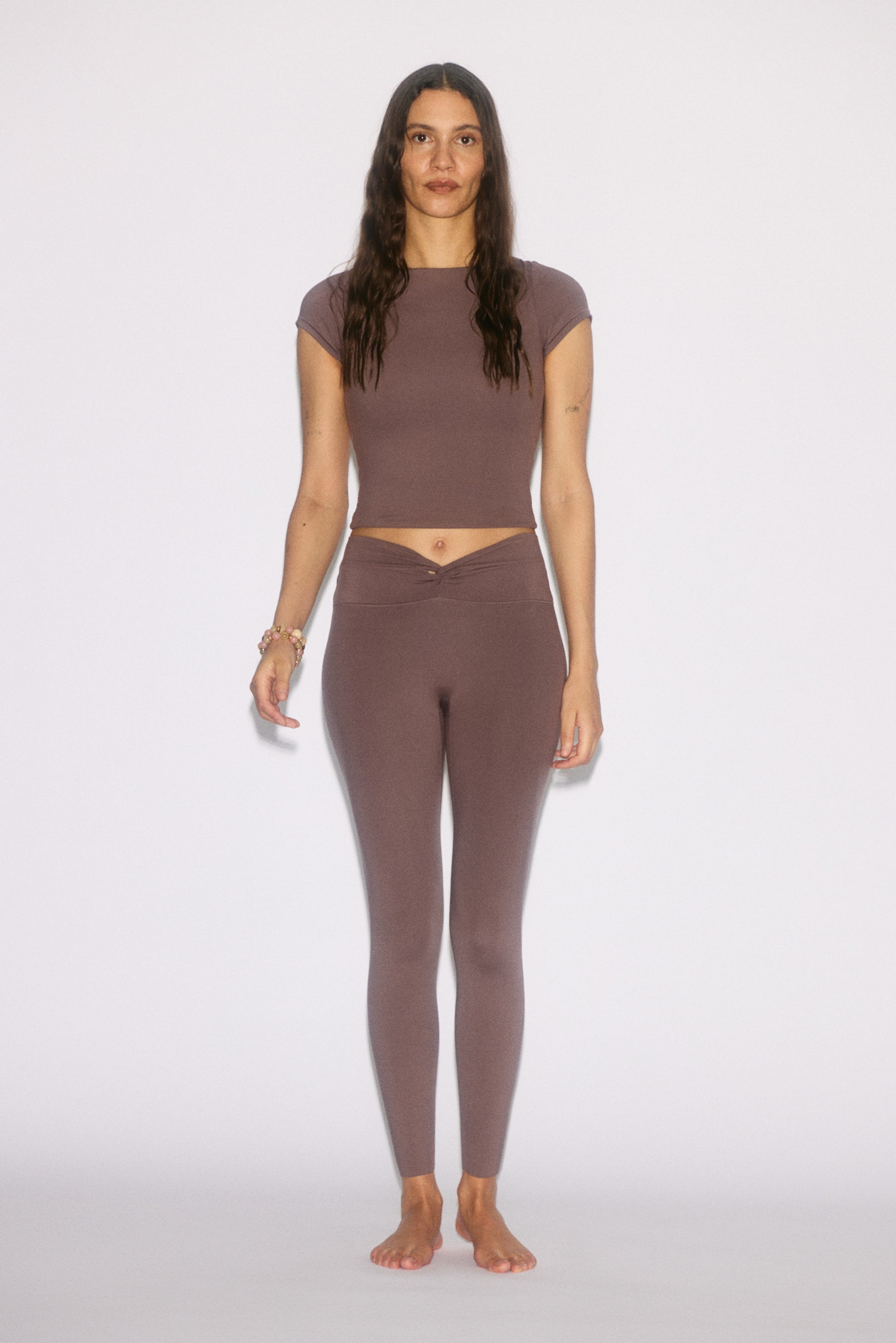 Xem ảnh lớn hơn: Quần legging thể thao với chất liệu SoftMove? màu nâu ánh tím đang được người mẫu mặc. Quần legging có chi tiết thắt eo xoắn và dáng ôm sát dài đến mắt cá chân, kết hợp hoàn hảo với áo crop top cùng màu cũng đang được mặc.