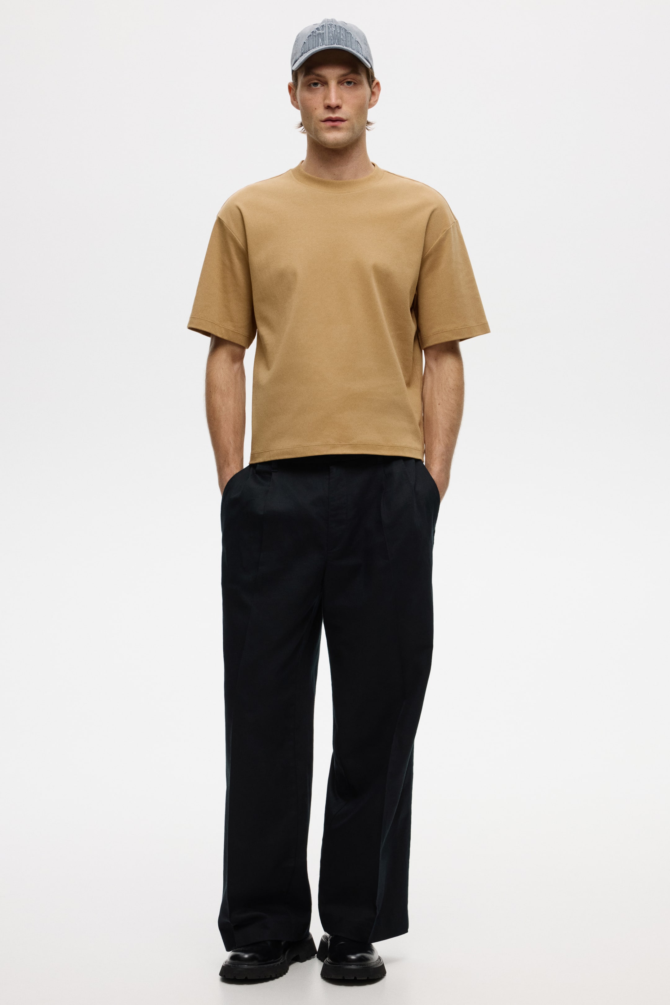 View larger image: A tan crew-neck T-shirt features a relaxed, boxy fit with short sleeves and a ribbed neckline. Dark-blue wide-leg trousers showcase front pleats and a high-waisted design, with the T-shirt tucked in.