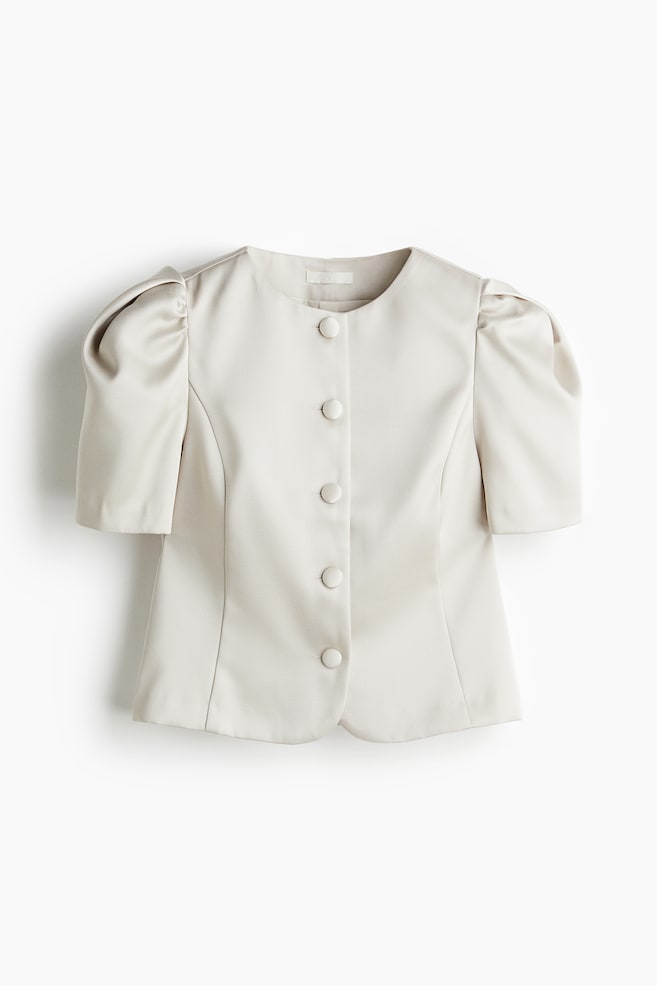 The FRONT of a short, fitted blouse, made of a smooth fabric with a subtle sheen, is displaying a round neckline, a front placket with six covered buttons, and short puff sleeves with pleats at the top. Princess seams are also running down the front panels. - 1