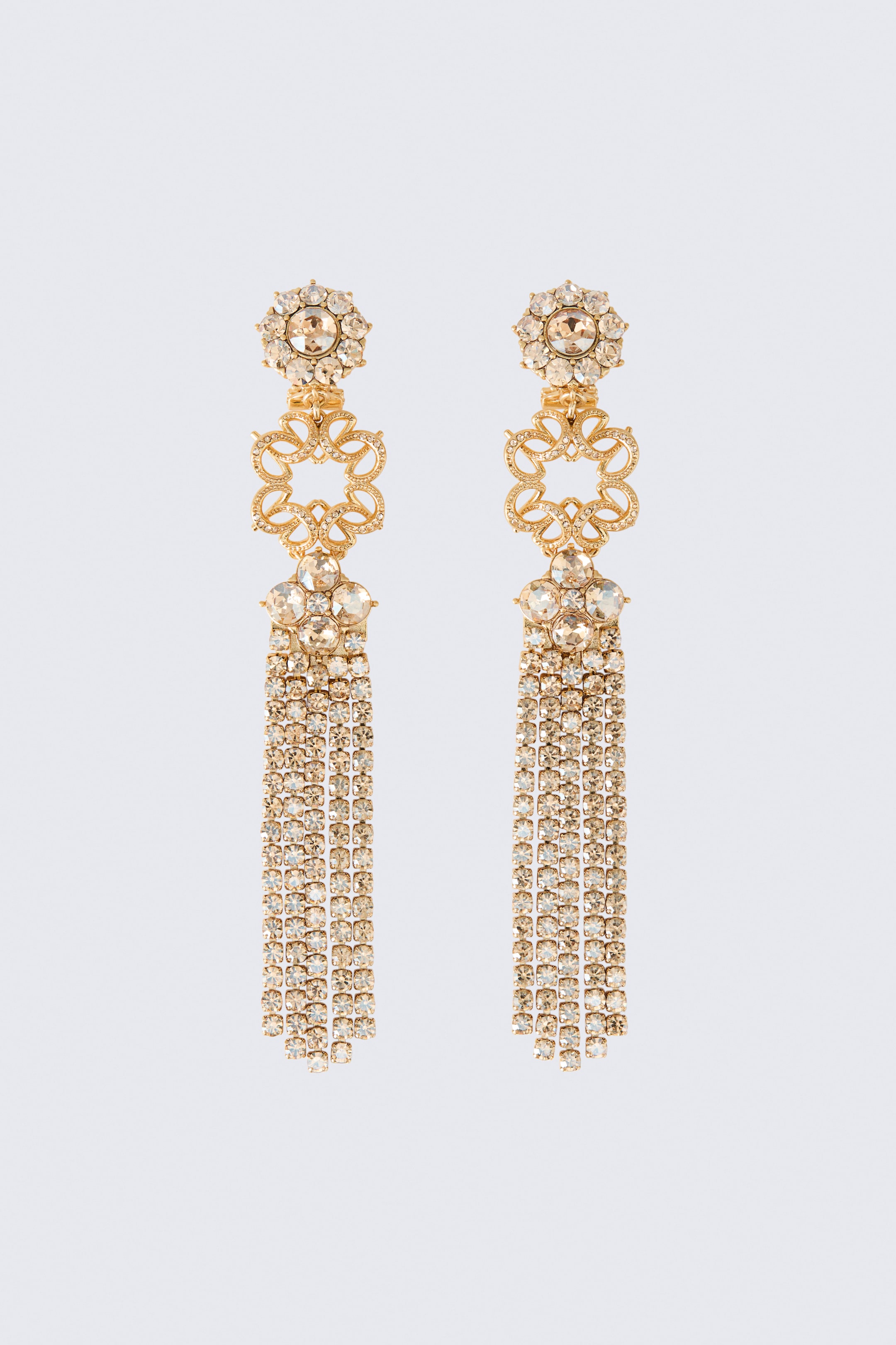 View larger image: A pair of long, gold-toned drop earrings is shown from a front angle, featuring round rhinestone-embellished studs at the top. Each earring displays a central openwork filigree monogram connecting to a cluster of larger rhinestones, from which multiple long, dangling rhinestone chain pendants suspend to form a glittering fringe.