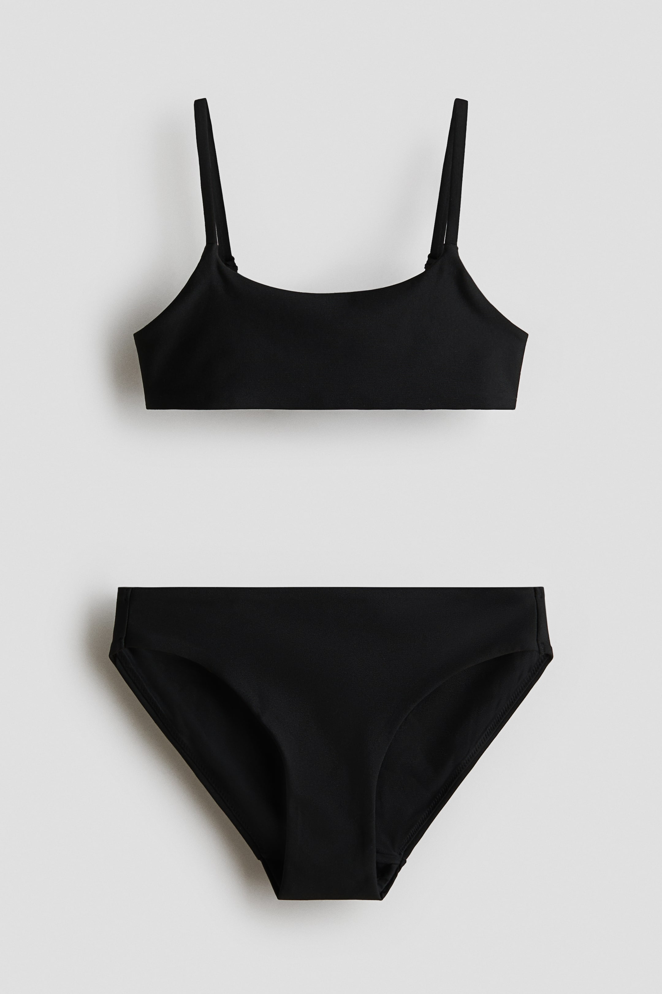 Grotere afbeelding bekijken: Een zwarte tweedelige bikini wordt frontaal getoond. Het bovenstuk heeft dunne schouderbandjes en een ronde halslijn, terwijl het onderstuk een bijpassende slip is.