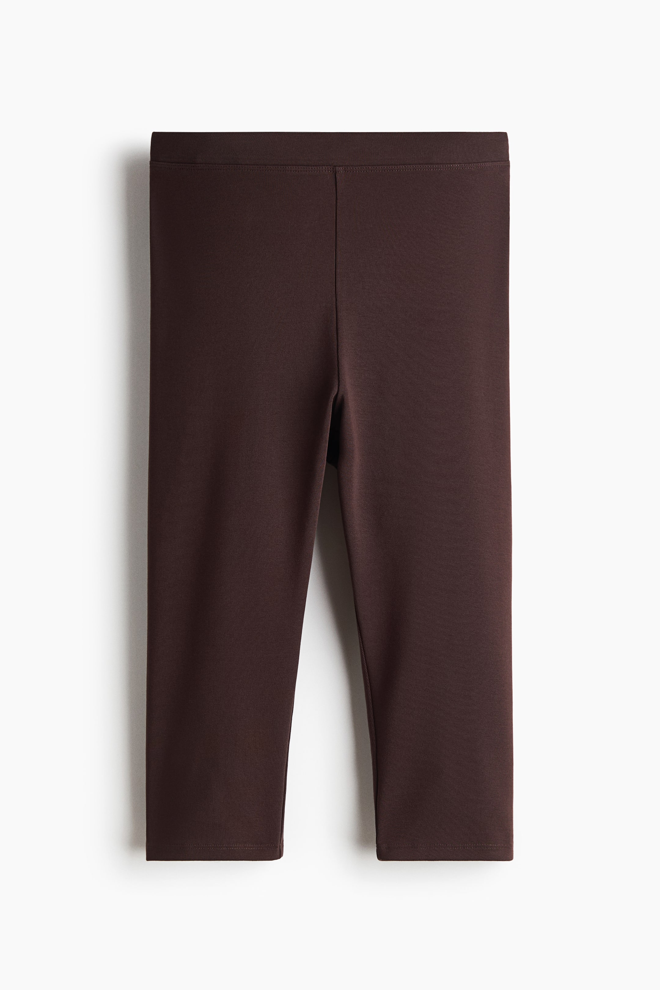 View larger image: Dark brown cropped leggings are shown from the front, highlighting a wide, flat waistband and a smooth, stretchy fabric, with a visible seam running down the center front of each leg.