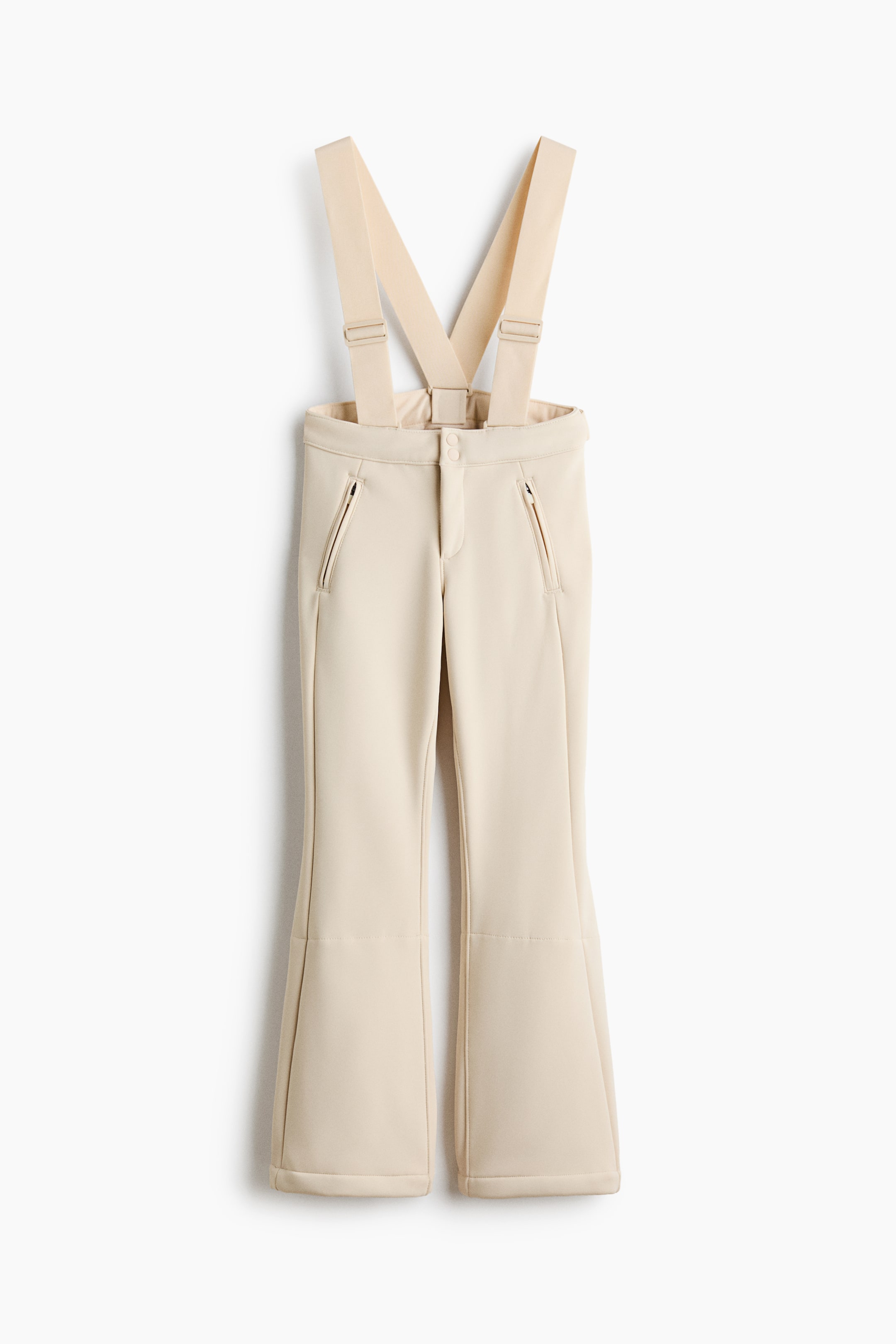 Ampliar la imagen: Pantalones de esquí de felpa afelpada en color crema claro, vistos de frente, con tirantes elásticos ajustables y cintura alta con cierre de broche a presión. El diseño muestra bolsillos inclinados con cierre de cremallera a la altura de la cadera y puños estructurados ligeramente acampanados en el bajo.