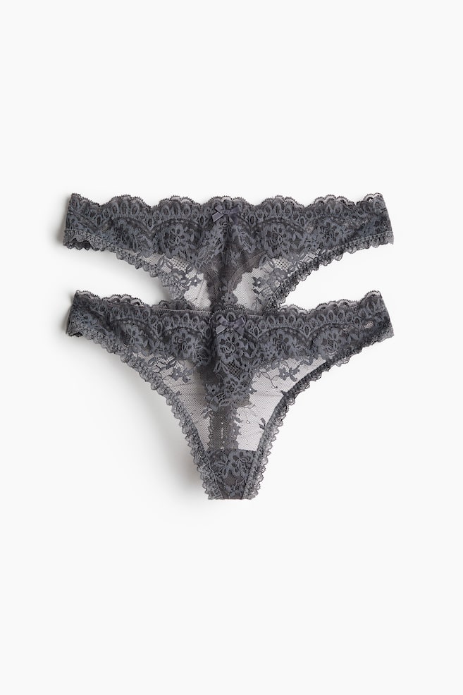 Two dark grey G-strings in sheer lace are lying flat in a front view, showcasing their low-rise design with scalloped edges and a small decorative bow at the centre waistband. - 1