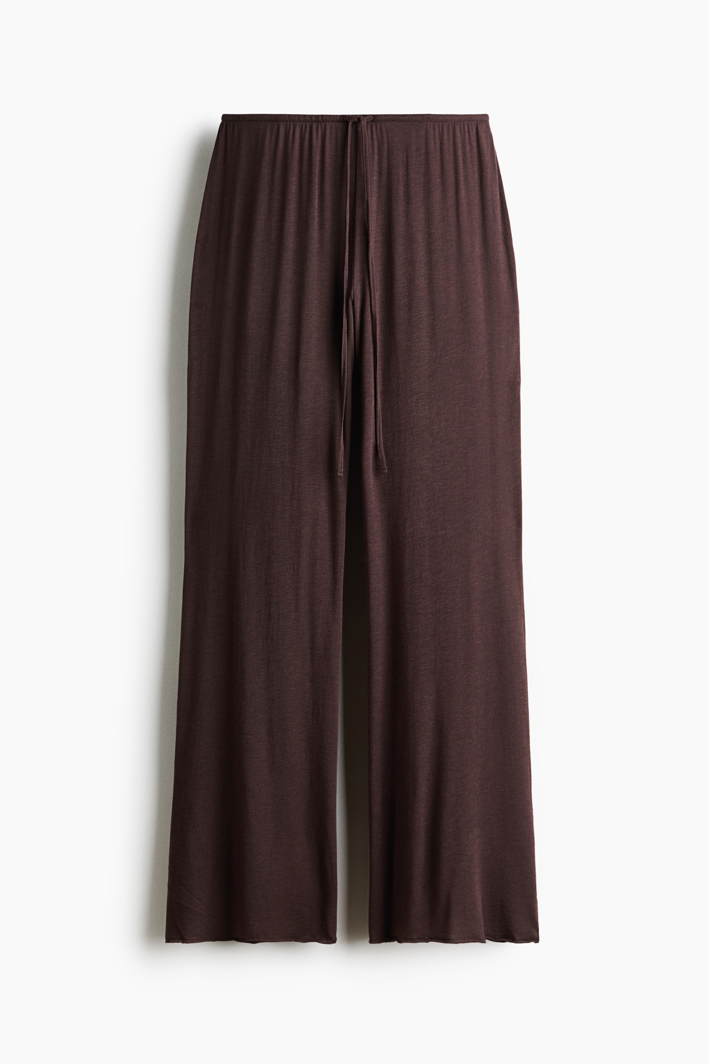 Dark brown jersey trousers featuring an elasticated waistband with a drawstring tie and relaxed, straight legs are worn by the model. The trousers are styled with a matching long-sleeved top in the same soft fabric.