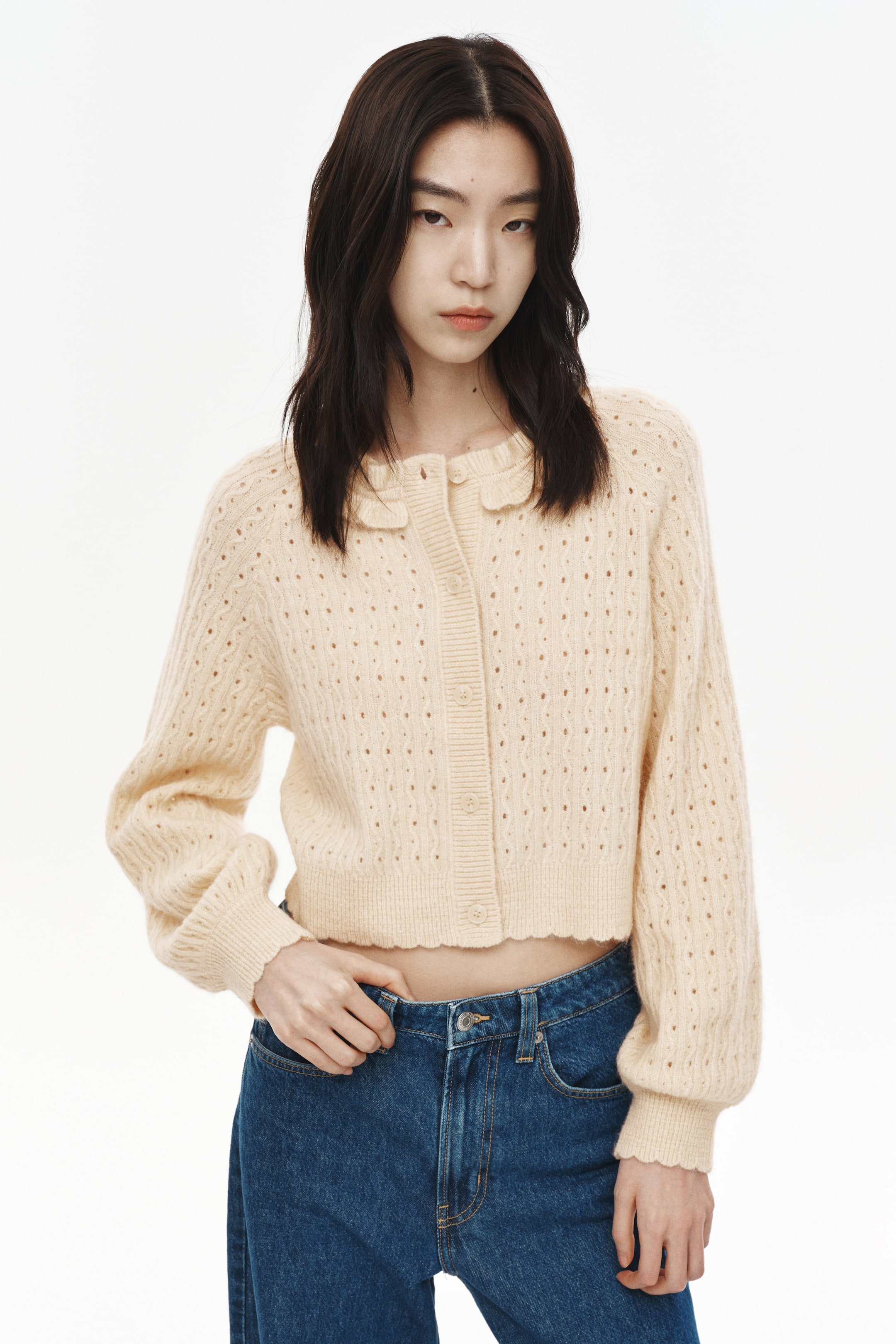 이미지 확대 보기: 연한 노란색 크롭 가디건이 정면을 향하고 있으며, 스캘럽 칼라와 버튼업 앞면이 특징입니다. 몸통과 소매 전반에 포인텔 니트 패턴이 돋보이며, 리브드 커프스와 스캘럽 헴으로 마무리되었습니다.