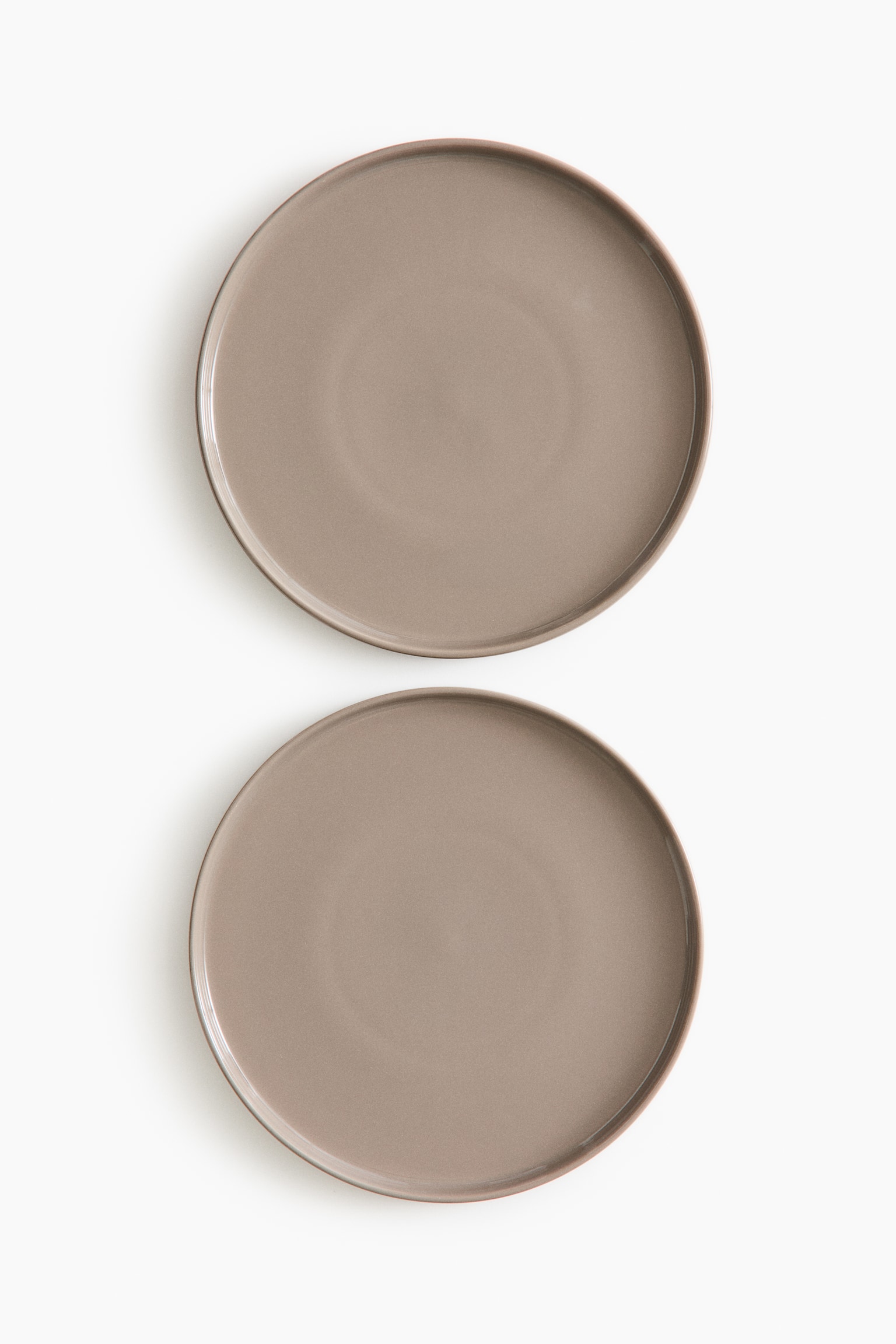 Δύο πιάτα μεσαίου μεγέθους από stoneware διαθέτουν γυαλιστερό, απαλό φινίρισμα σε taupe. Κάθε πιάτο έχει στρογγυλό σχήμα με διακριτικά υπερυψωμένο χείλος.