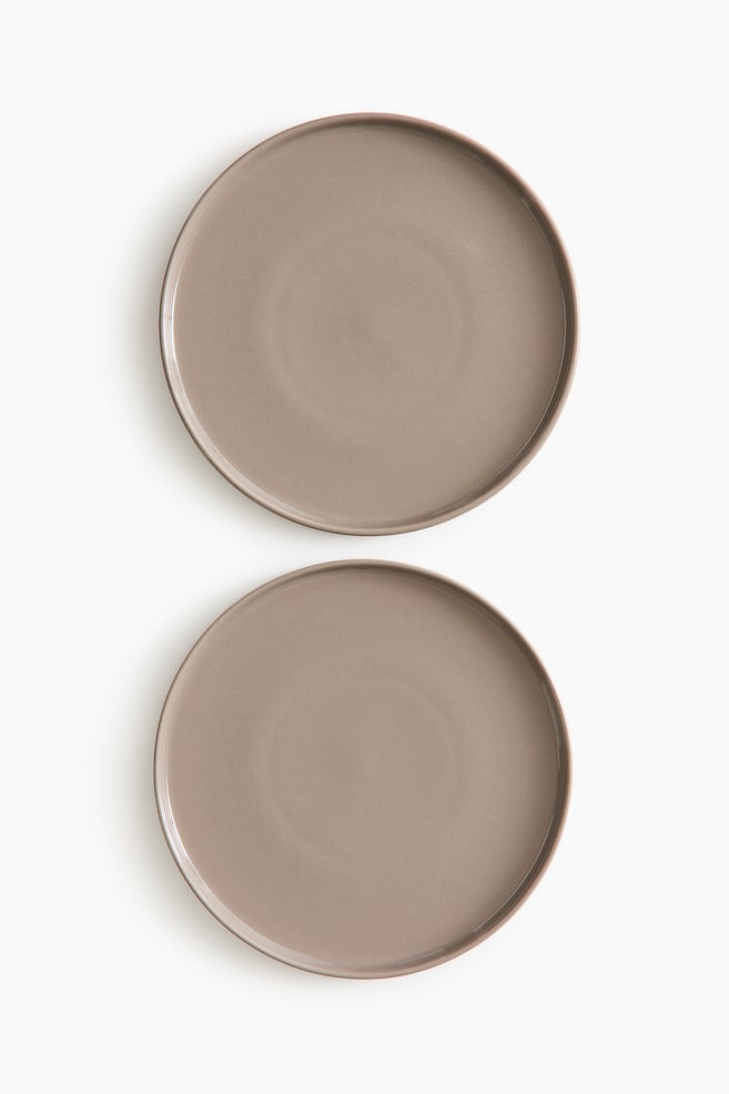 Two mid plates in stoneware are featuring a glossy, muted taupe finish. Each plate is presenting a round shape with a subtly raised rim. - 1