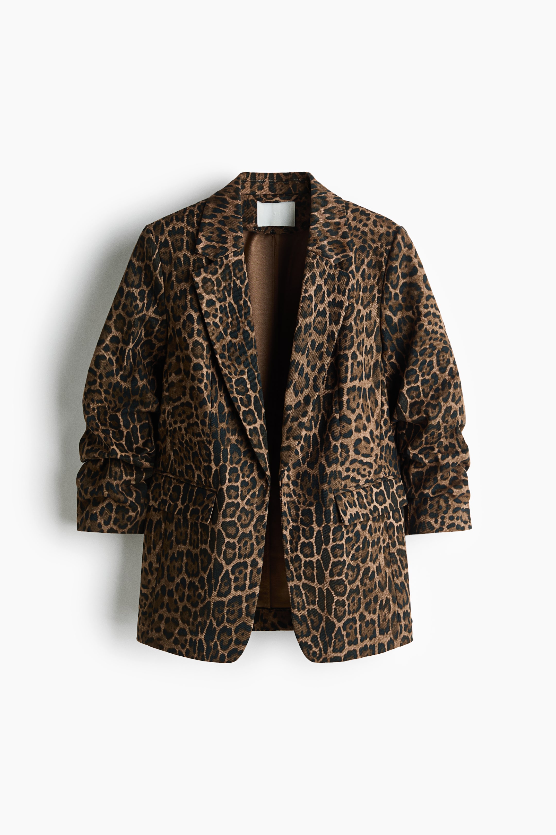 Vis større bilde: En blazer med leopardmønster er vendt mot front og har jakkeslag med hakk, markerte skuldre og en åpen front uten lukking. Plagget har rynkede ermer i trekvart lengde og to innfelte lommer foran med klaffer.