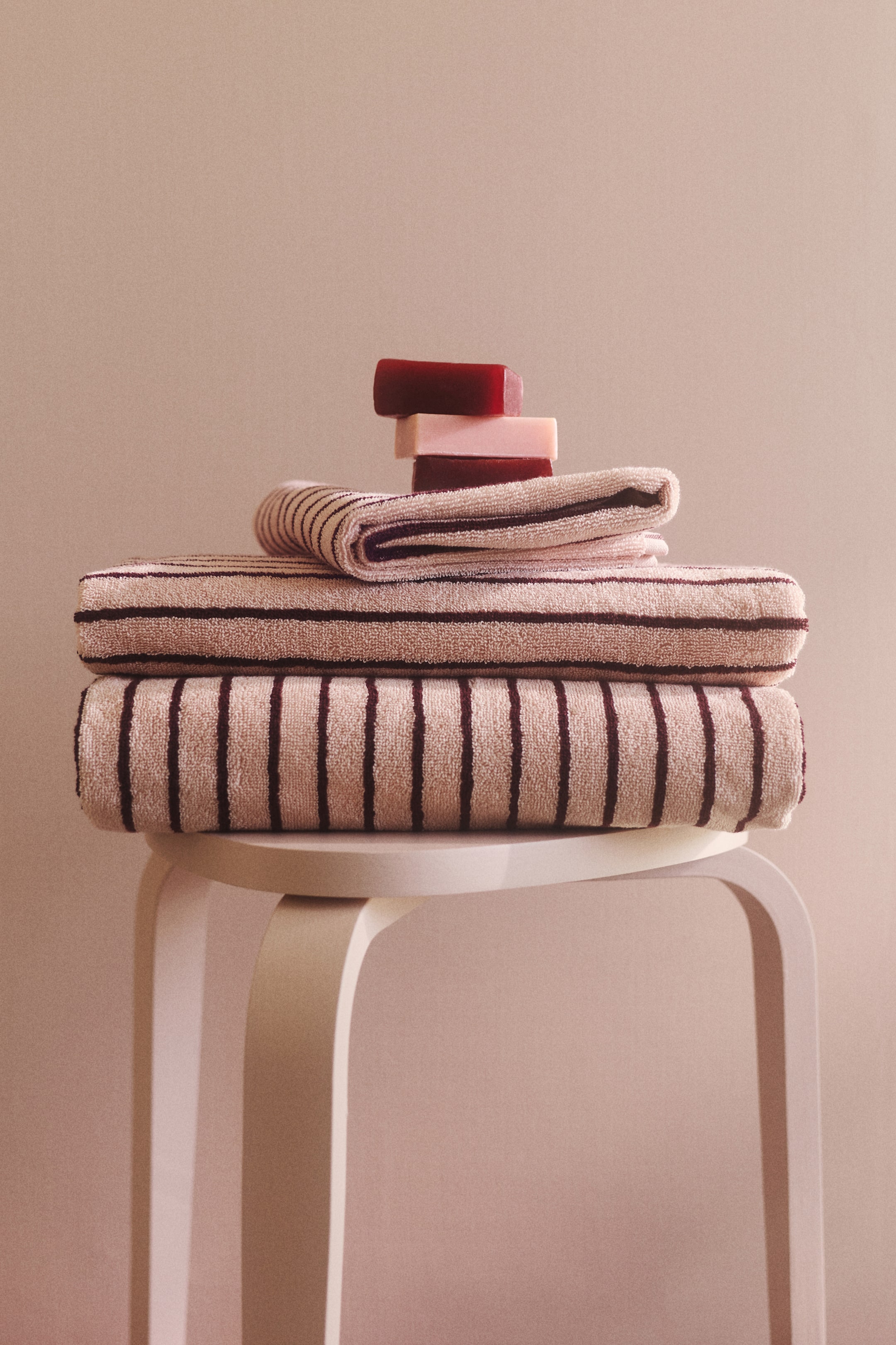 Ver imagen más grande: Las toallas de baño con textura de rizo de algodón están apiladas y dobladas, mostrando rayas teñidas en hilo de color marrón oscuro sobre un fondo beige claro, con tres barras de jabón descansando sobre la toalla superior.