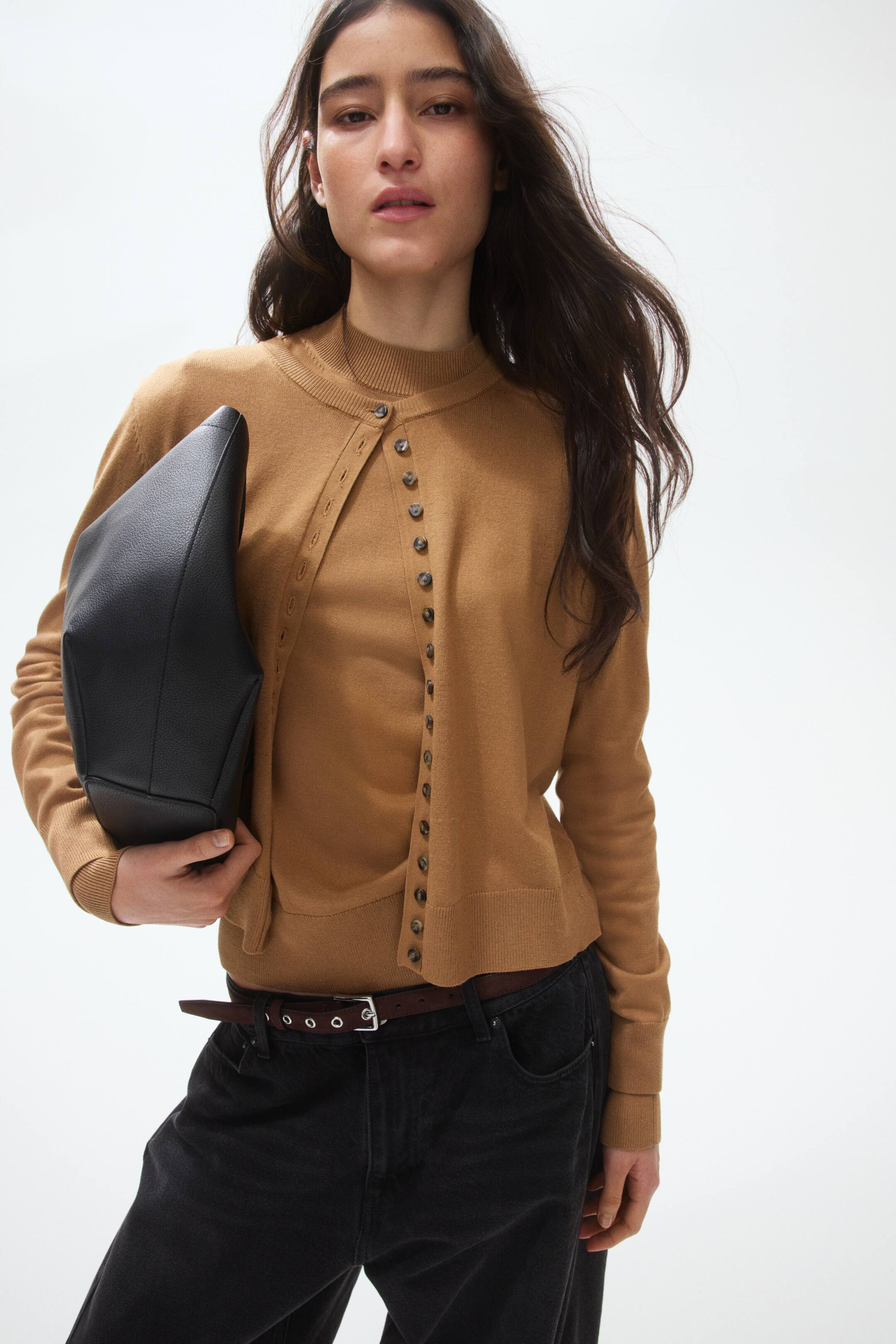 View larger image: A camel-coloured knitted cardigan featuring an asymmetric button-front closure with dark buttons, a mock neck, long sleeves with ribbed cuffs, and a ribbed hemline.