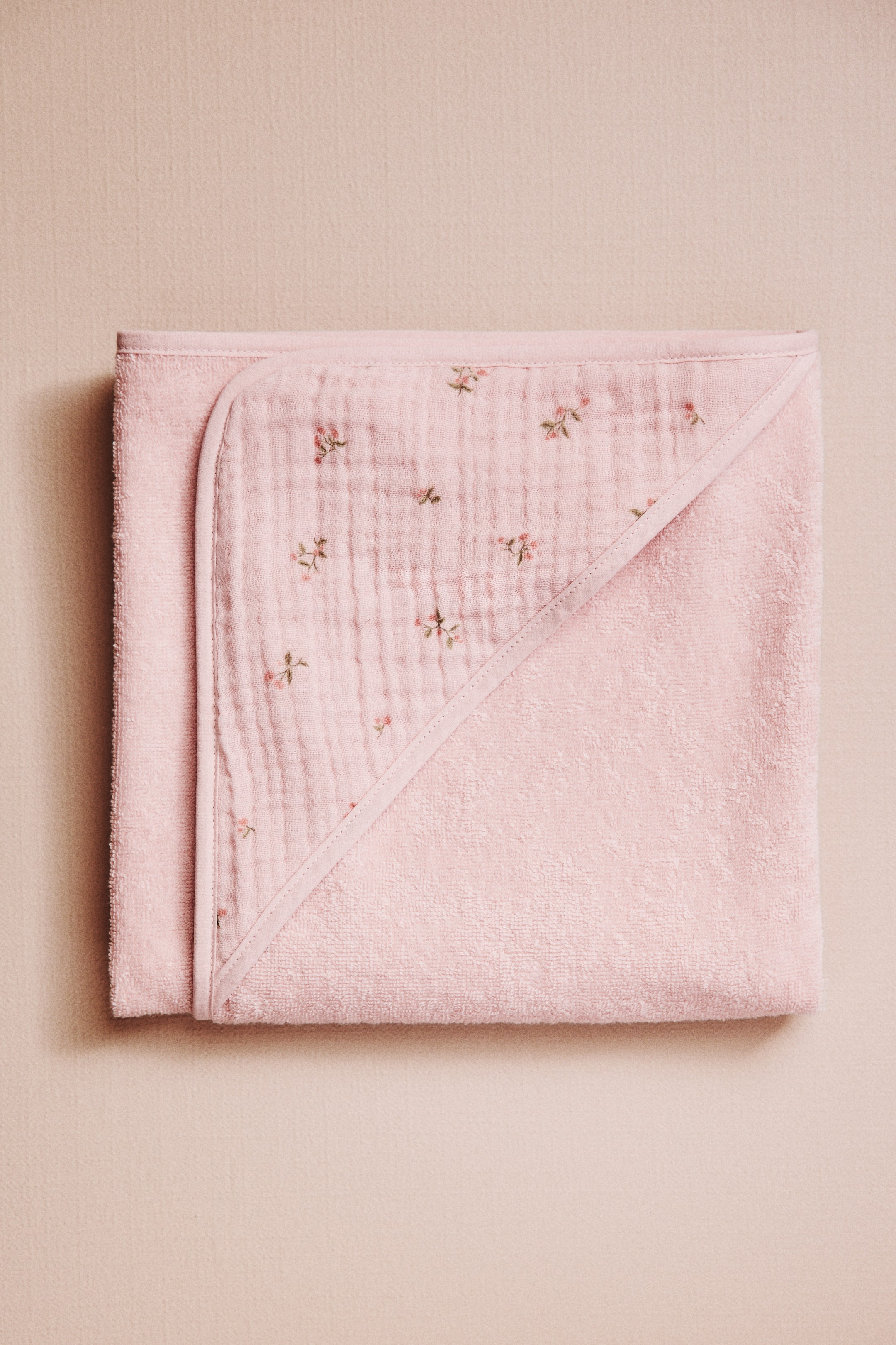 Ampliar la imagen: Una toalla de bebé con capucha rosa está extendida, vista desde el frente. Su cuerpo principal está hecho de suave tela de toalla, y una capucha triangular de muselina muestra un delicado patrón floral.