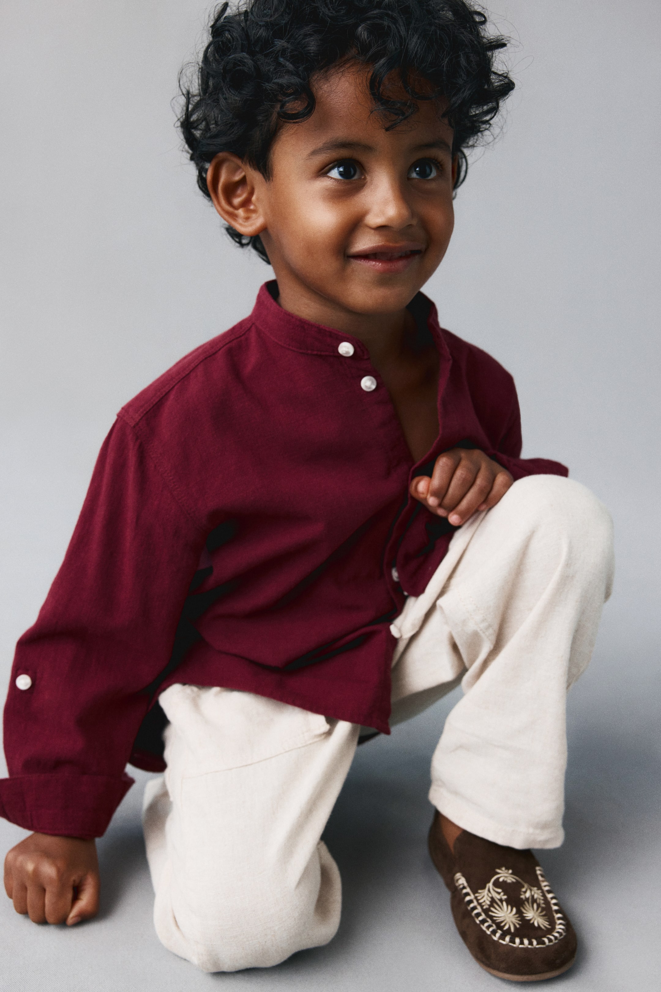 View larger image: A dark red, long-sleeved shirt in a soft, airy weave is worn from the front, featuring a band collar and a button-down front with white buttons. The shirt showcases long sleeves with buttoned cuffs and a side tab-and-button detail designed for rolling up.