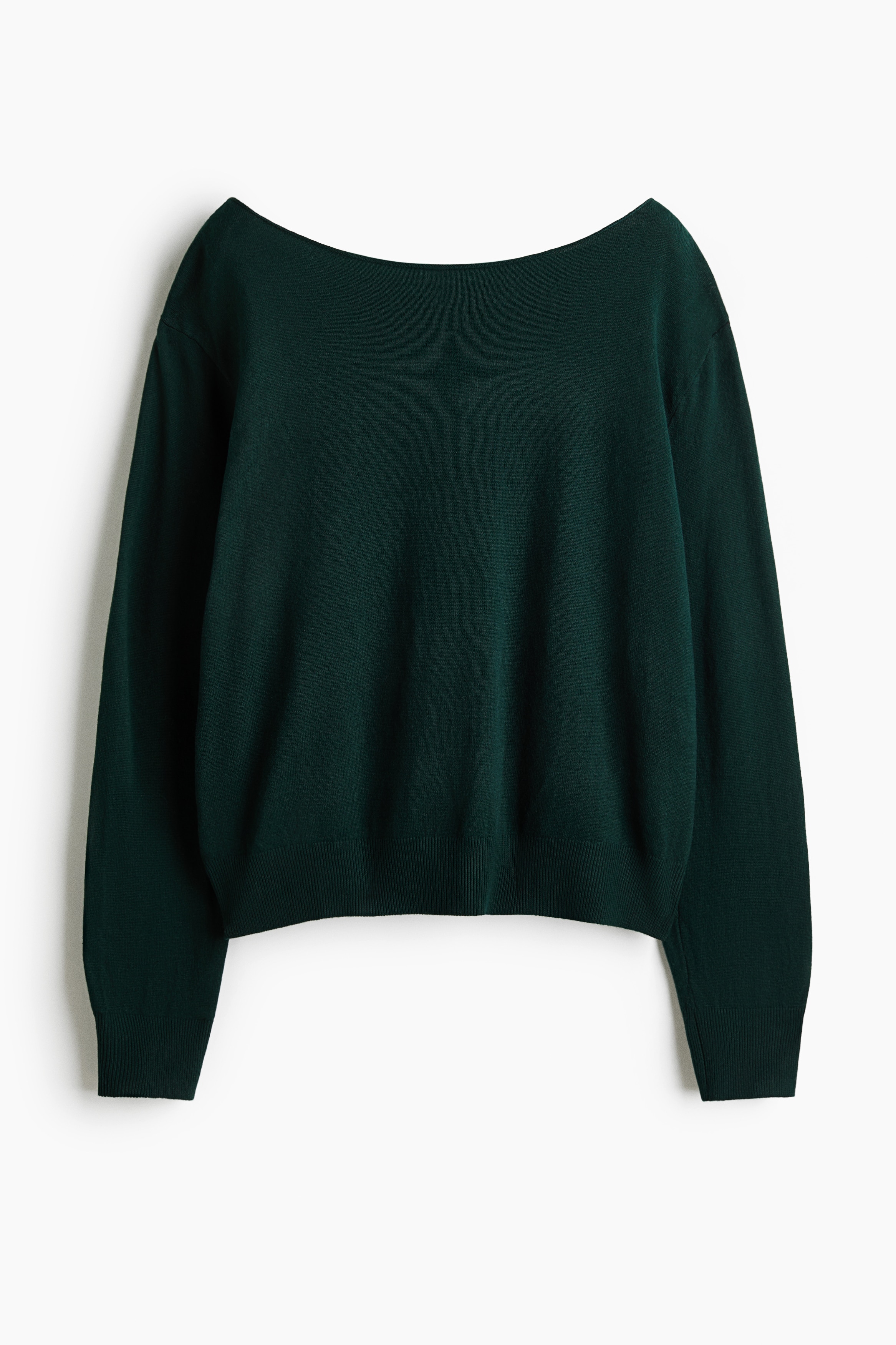 A dark green, off-the-shoulder knit jumper featuring a rolled-edge neckline, dropped shoulders, and ribbed cuffs is being worn by the model. The jumper is styled with light-wash, wide-leg denim jeans and cream sneakers.