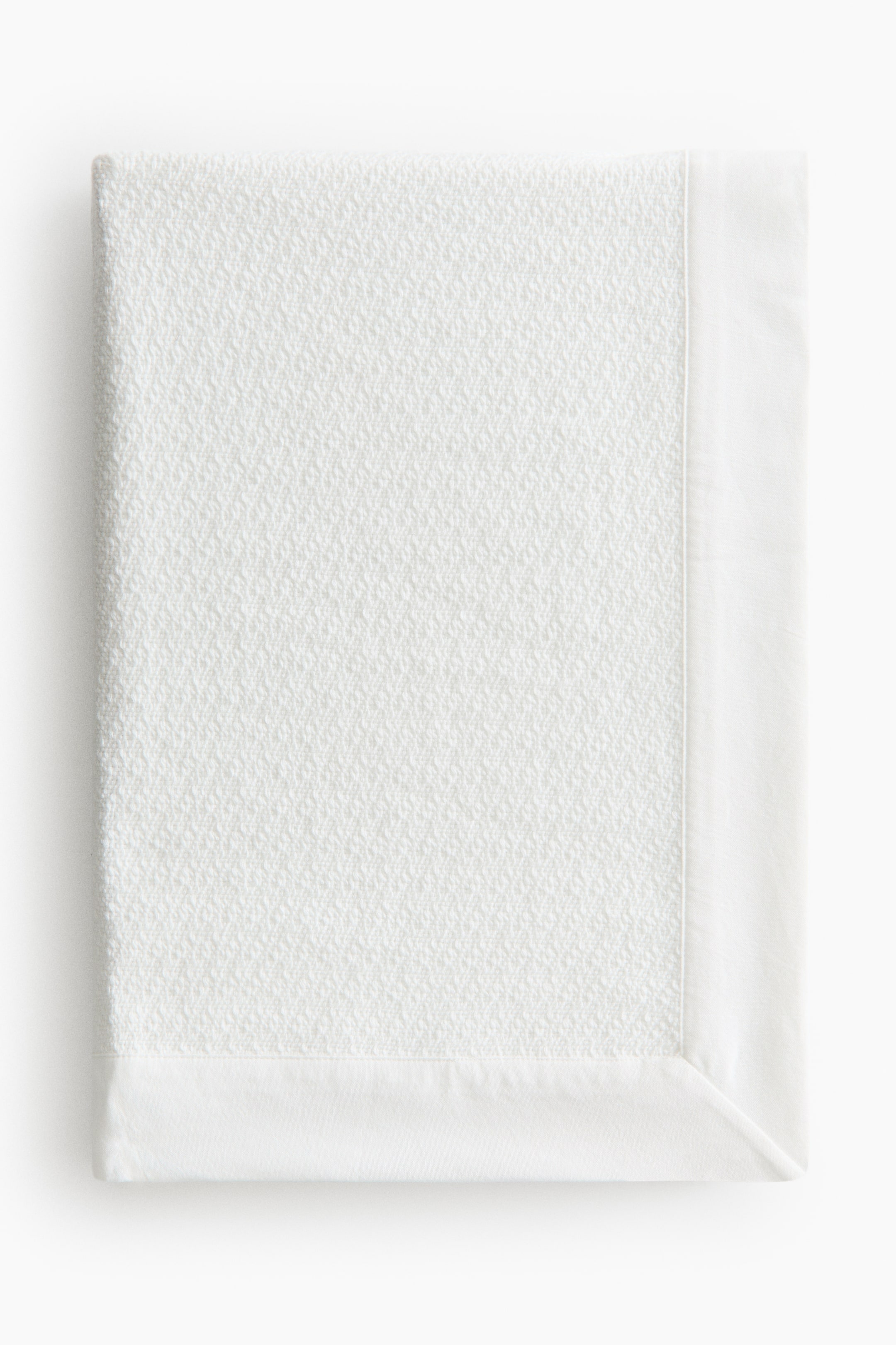 View larger image: A white blanket displays a subtly textured weave across its main body, featuring a smooth, flat border along the right and bottom edges.