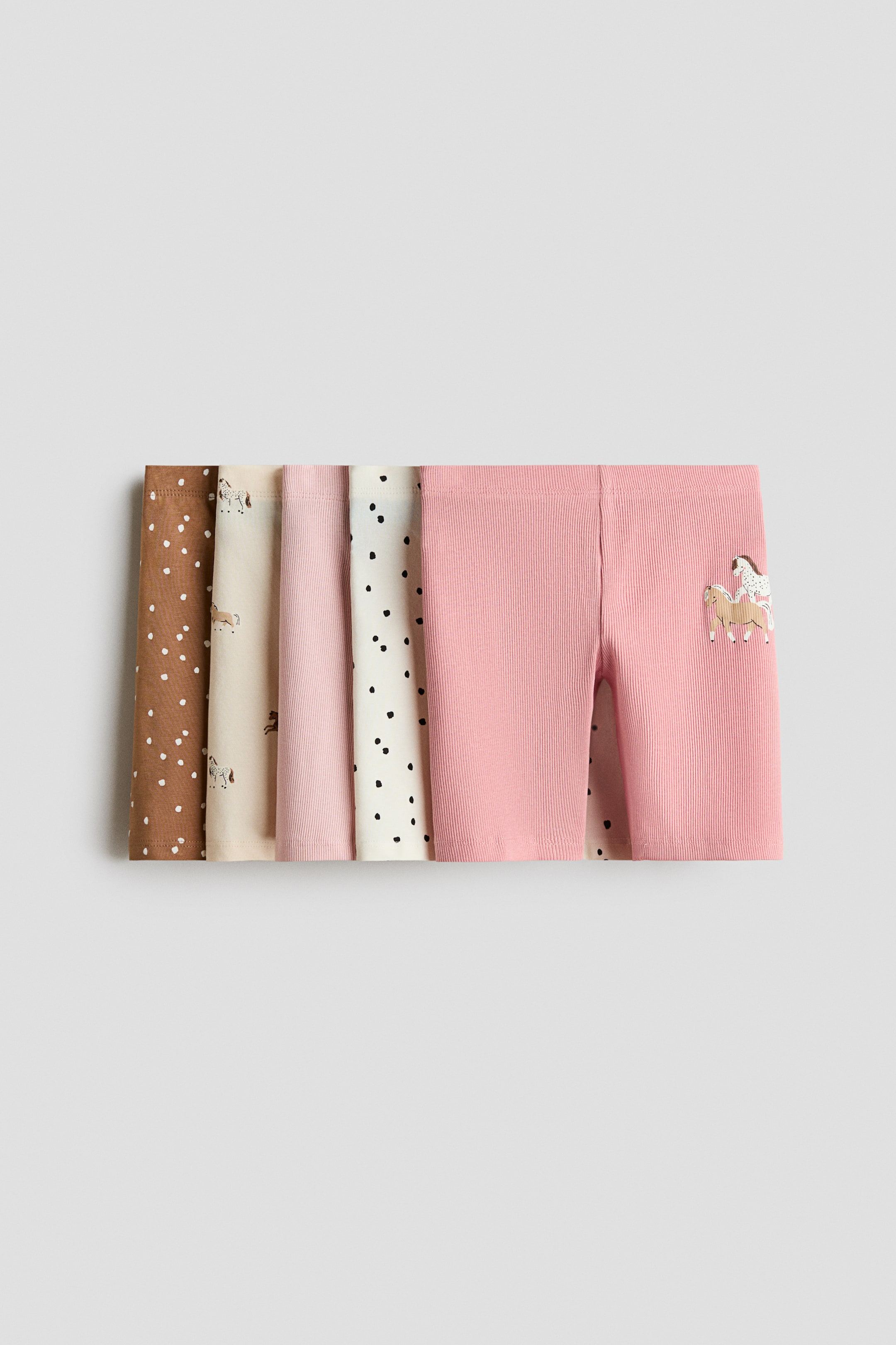 View larger image: A set of five pairs of ribbed knit shorts is laid flat in an overlapping row, showcasing a variety of colors and patterns. The front-facing pair is solid pink with a small horse graphic on the lower leg, while the other pairs layered behind feature brown with white dots, beige with horse illustrations, solid light pink, and off-white with black dots.