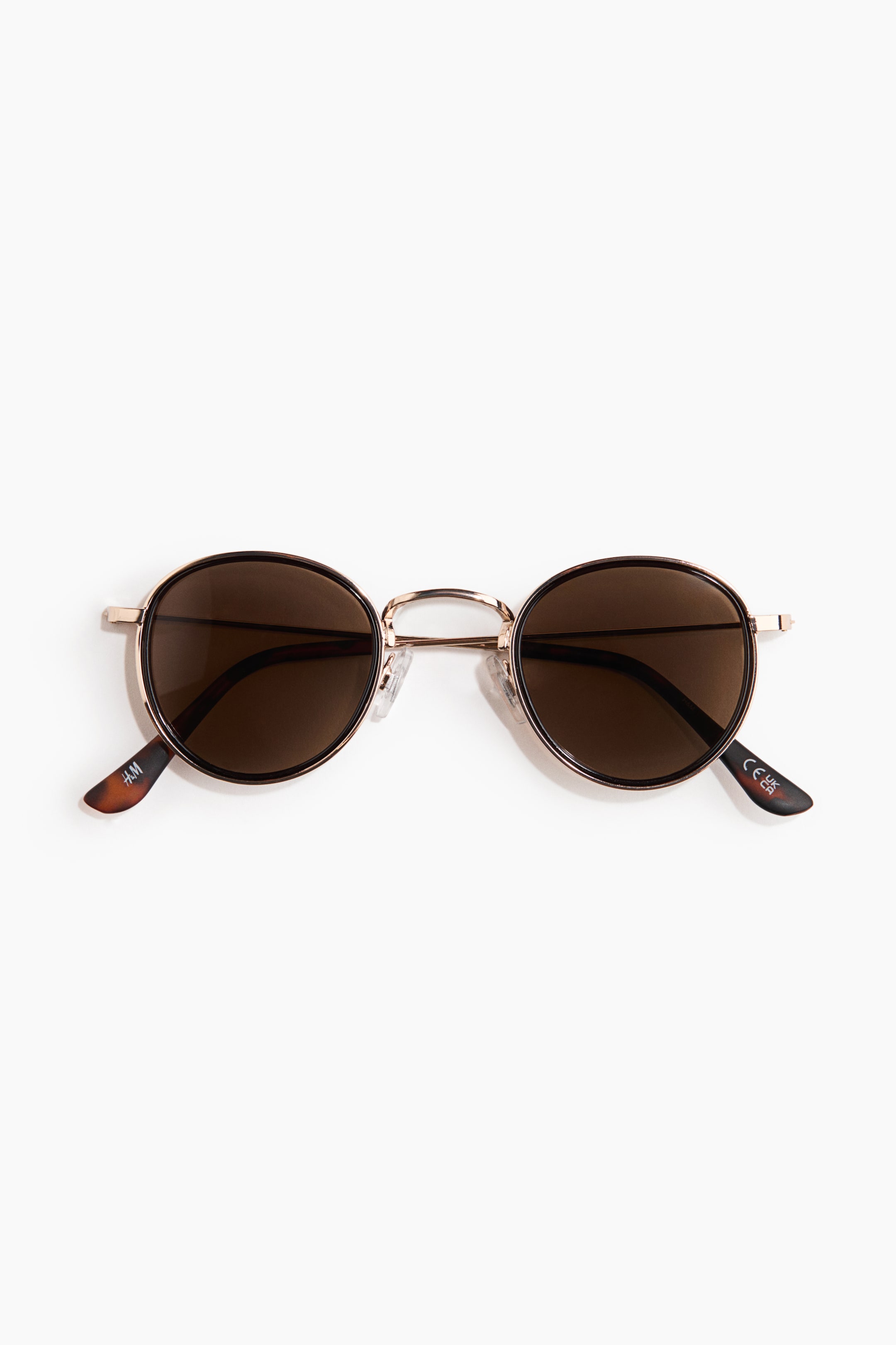 View larger image: Sunglasses are positioned frontwards, showcasing round brown lenses encased in slender metallic gold-toned frames with a darker outer rim. Transparent nose pads provide support to the bridge, while the delicate metallic temples conclude in brown tortoise shell tips.
