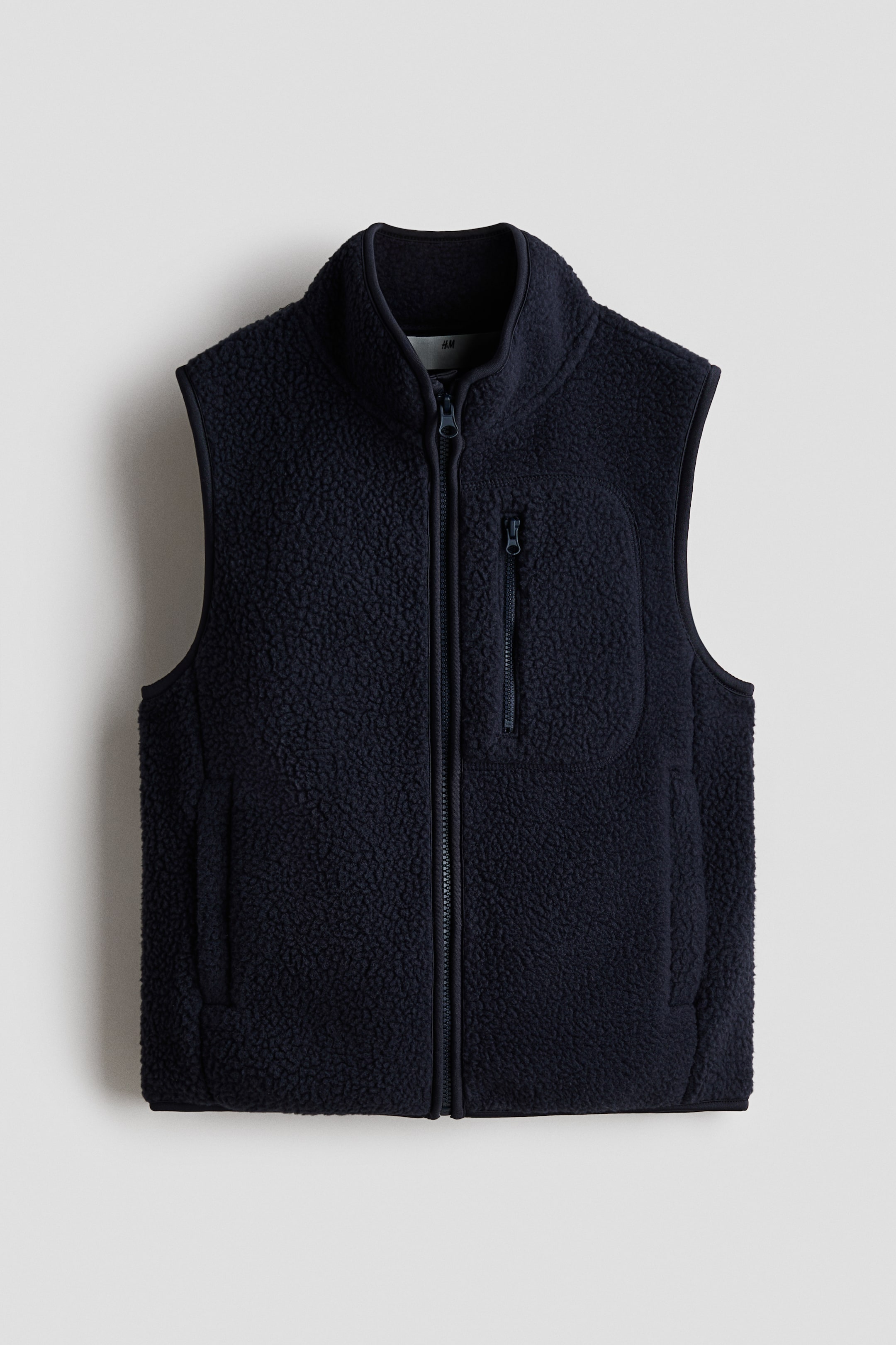 Größeres Bild anzeigen: Ein dunkelblaues, weiches Teddy-Gilet präsentiert sich von VORNE, mit einem Stehkragen, einem Reißverschluss entlang der Vorderseite, einer Brusttasche mit Reißverschluss und seitlichen Leistentaschen mit Reißverschlüssen.