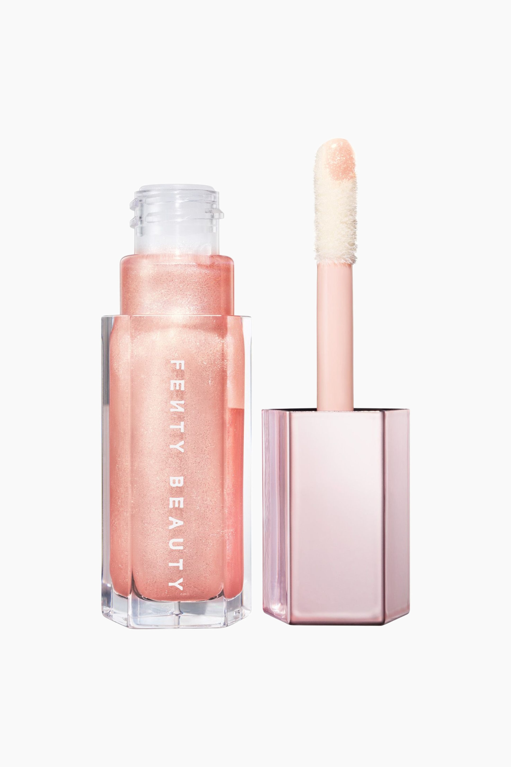 Visa större bild: En klar, hexagonal flaska fylld med ett skimrande persiko-rosa läppglans står upprätt och visar den vertikala vita ”FENTY BEAUTY”-logotypen på framsidan. Bredvid den står den metalliskt blekrosa hexagonala korken, som håller sin stora, fluffiga doe-foot-applikatorstav upprätt och visar den glansiga produkten på spetsen.