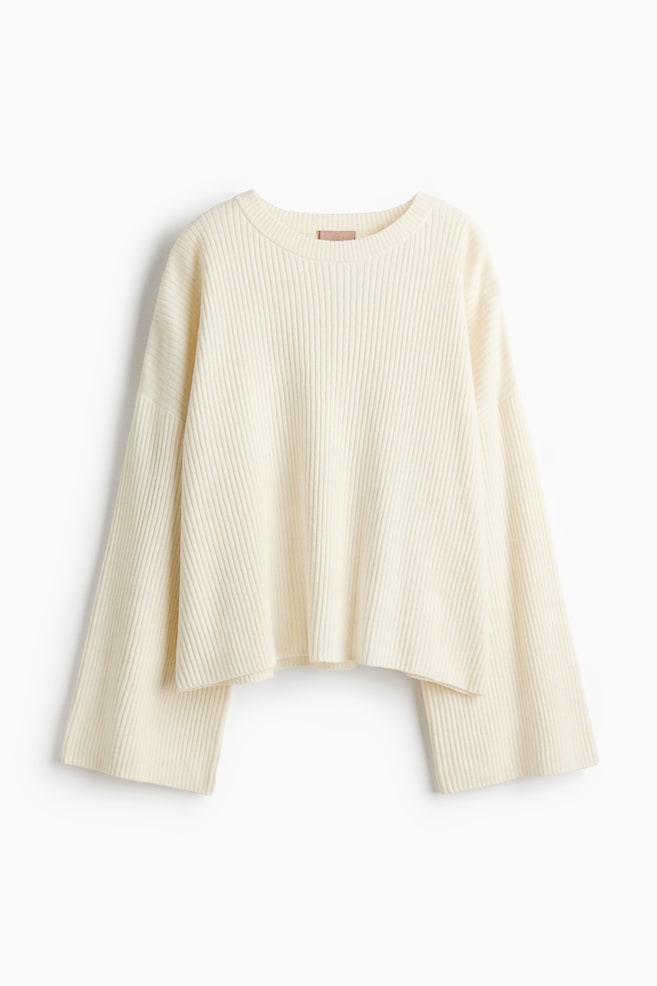 El jersey de punto acanalado en color crema presenta un cuello redondo y mangas anchas, mostrando un largo recortado y un ajuste relajado cuando se coloca plano y de frente. - 1